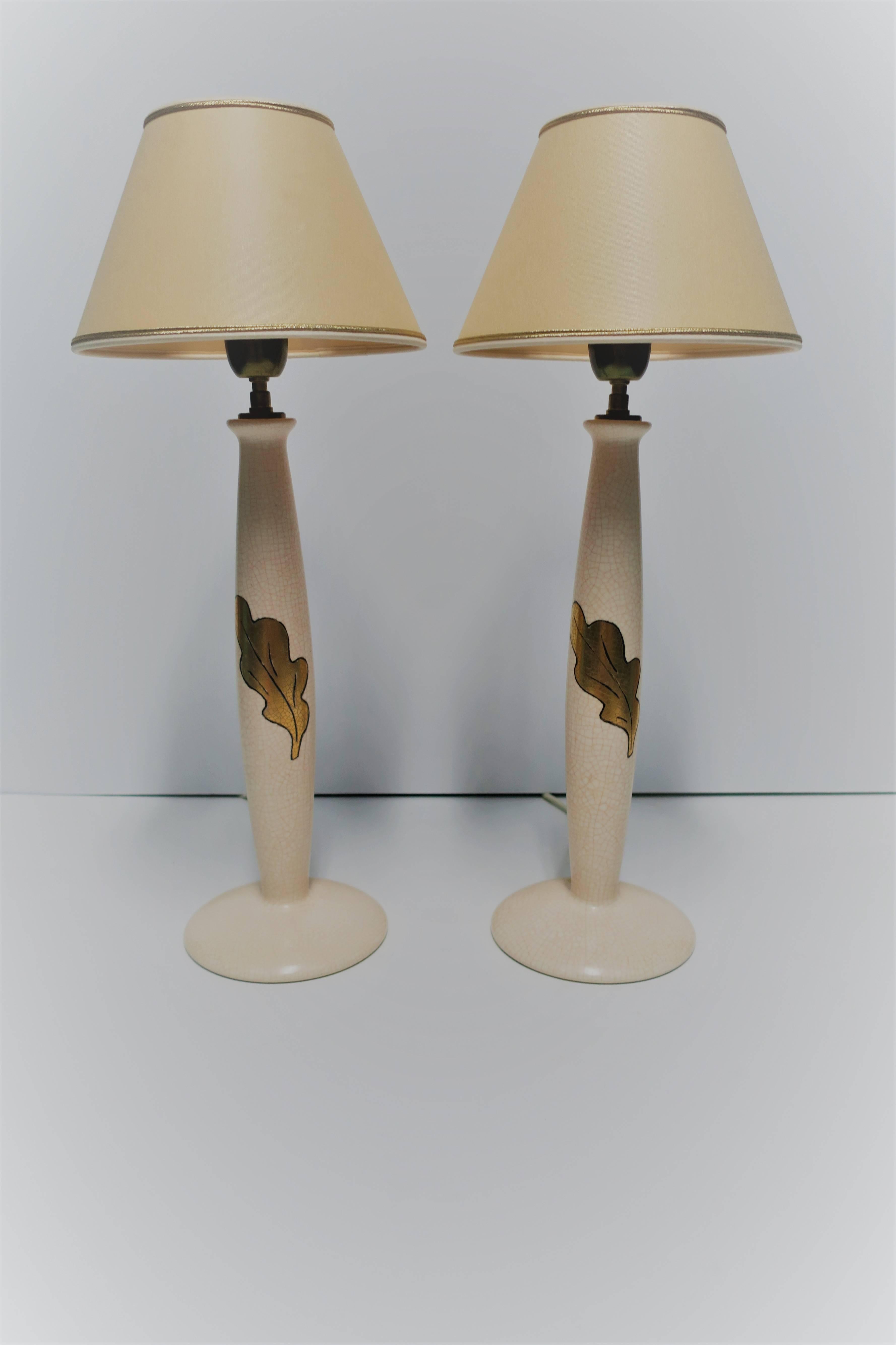 A beautiful pair of French desk or table lamps with gold acanthus leaf design. Lamps are a neutral/flesh tone/very light pink-peach hue with a 'crackle' ceramic and gold acanthus leaf outlined in black on front. Marked 