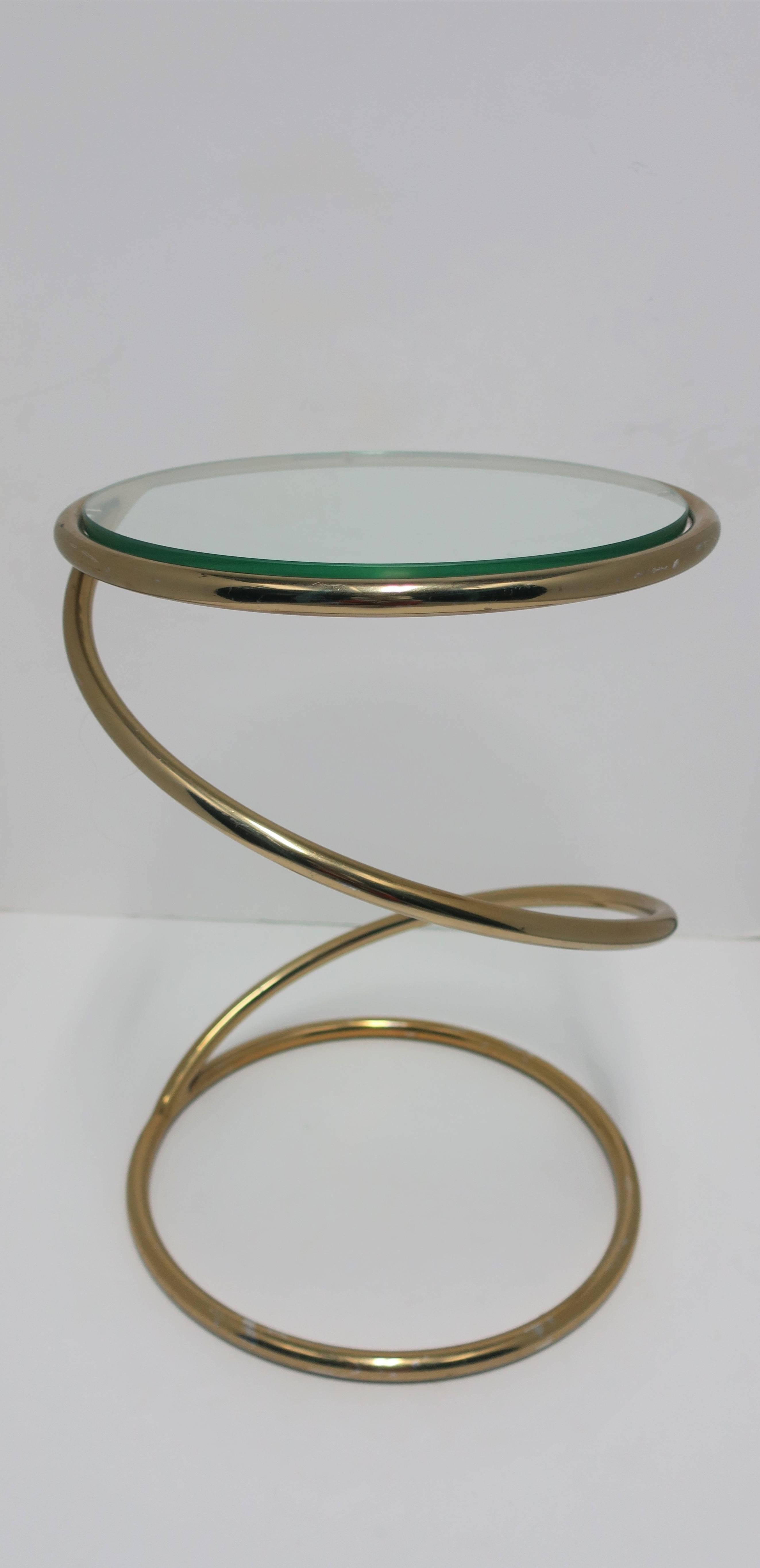 A vintage Modern round brass-plated and glass 'twist' side table after designer Milo Baughman, circa 1970s. Table has a 'twist' or 'spring' design with substantial glass top. Glass top is new and 'tempered'. 

Measurements include: 18.25 in. H x 13