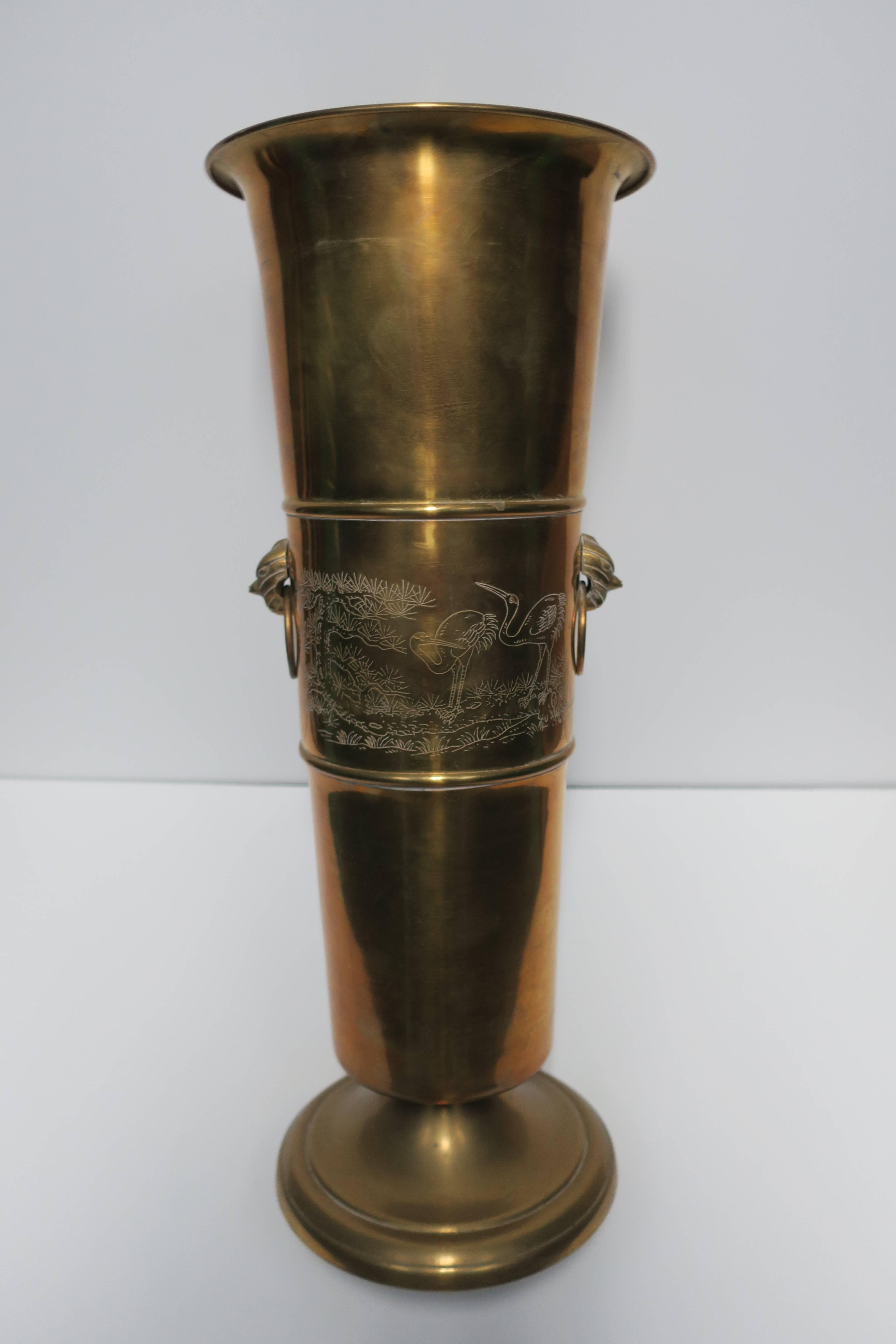 A vintage brass 'Urn' shape umbrella stand with decorative 'loop' sides and embossed decorative scenes on front (two embossed 'Stag's' or deer on one side, and two crane birds on the other.) 

Measurements include: 22.5 in. H x 9 in. Diameter.