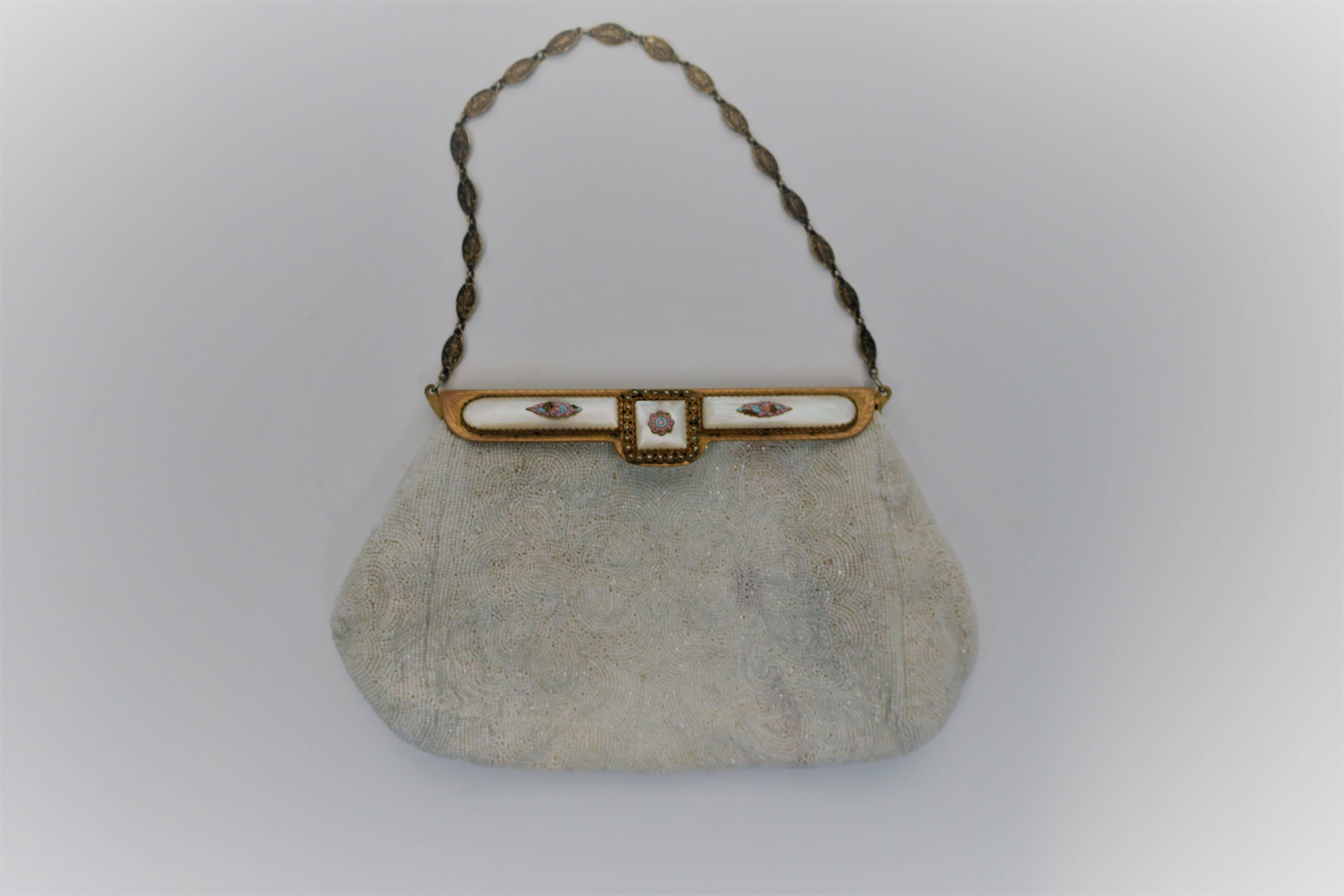 A beautiful vintage white beaded handbag with brass hardware decorated with Mother-Of-Pearl, pastel enamels and marcasite details, circa early to mid-20th century. Europe. Closure specifically is marcasite, pastel enamel of pink and blue, and