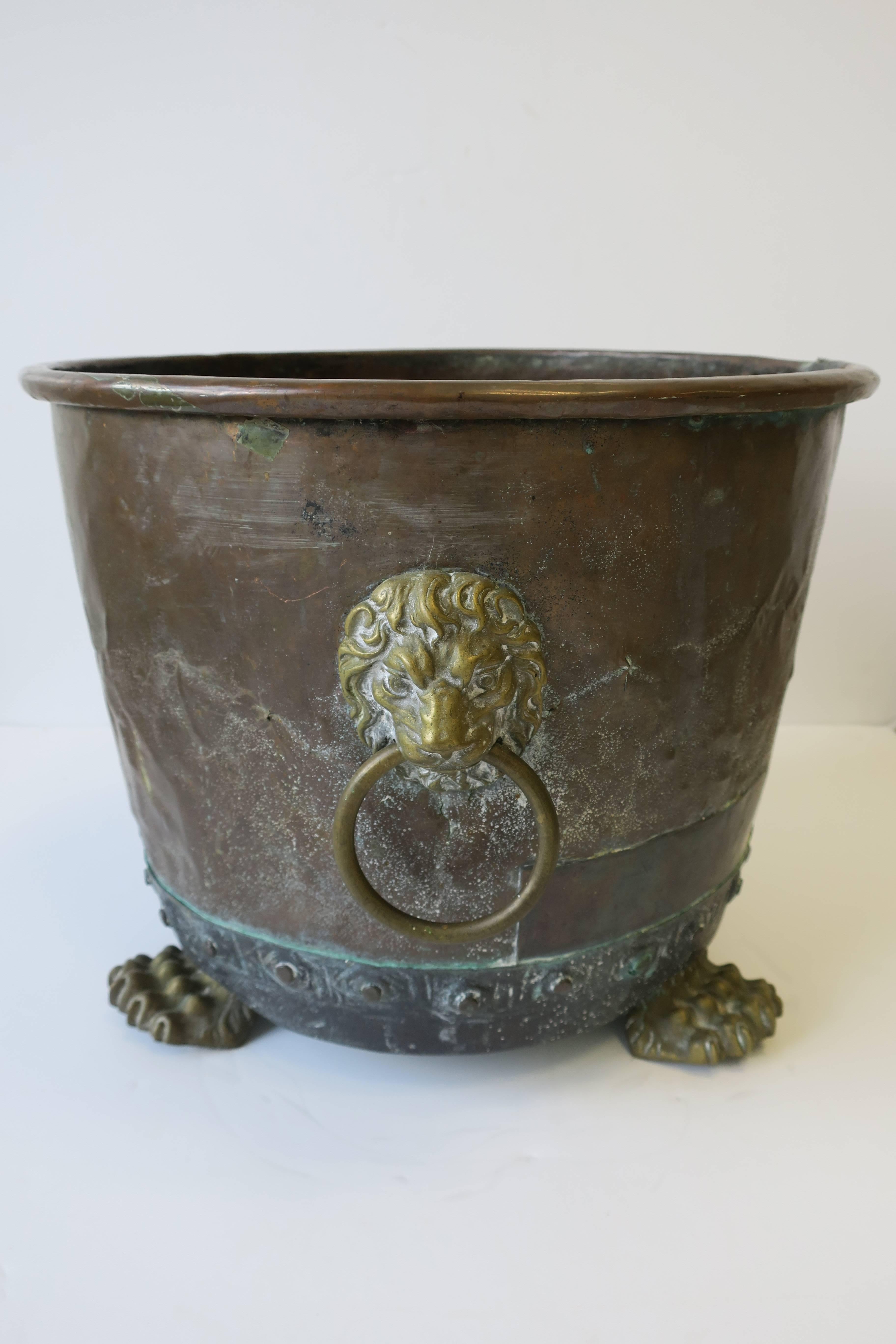 A beautiful and strong antique English brass and copper firewood log holder vessel with Lion details. Beautiful and detailed brass lion head's with ring loops and lion paw feet. Hardware details around base. Riveted construction with natural patina