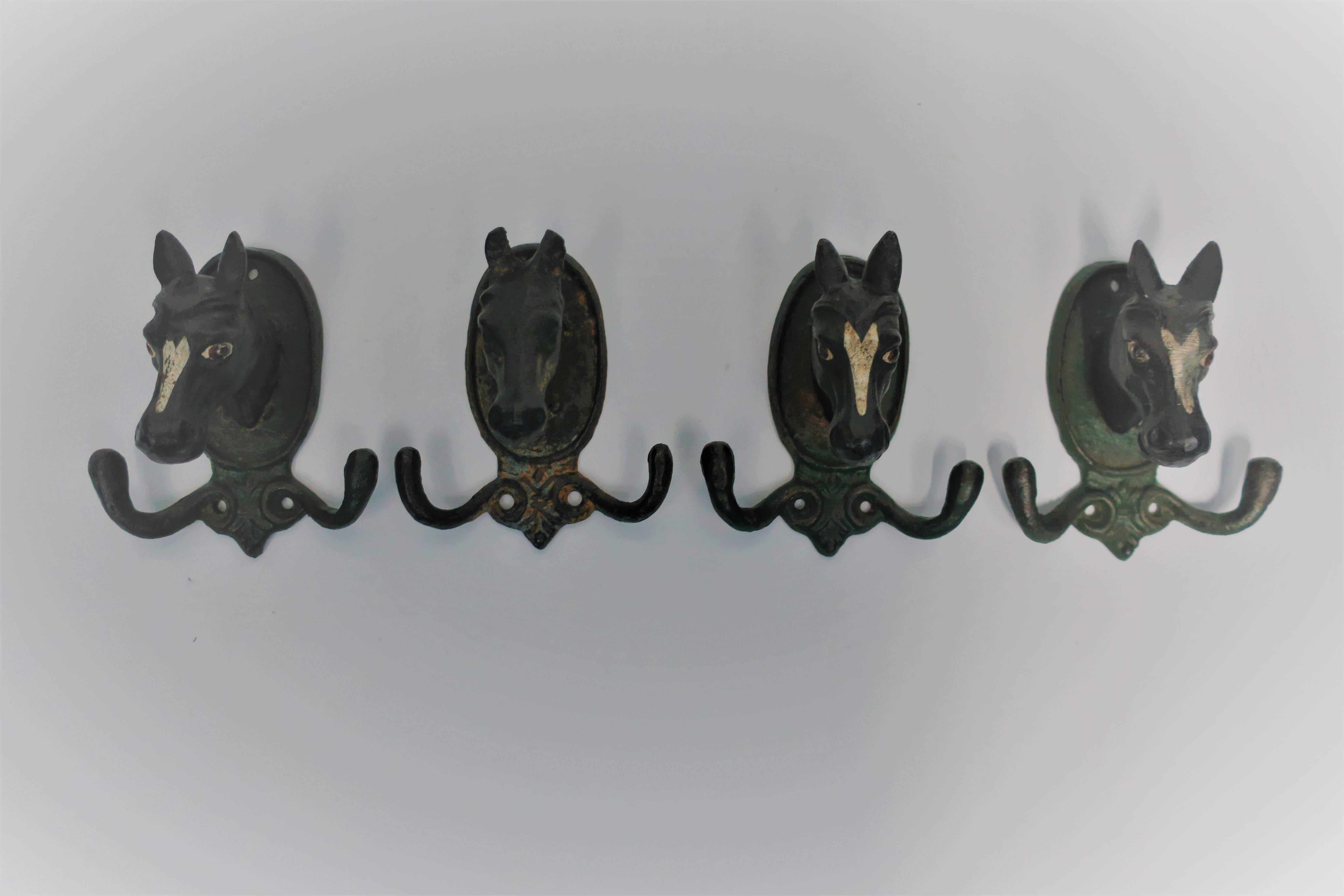 A set of four vintage horse or equine painted iron hardware wall hooks. Paint colors include white, black, and dark green. Two 'hooks' on either side of each. Each piece measures 4 3/8 inches high x 4 inches wide. Set available here online. By