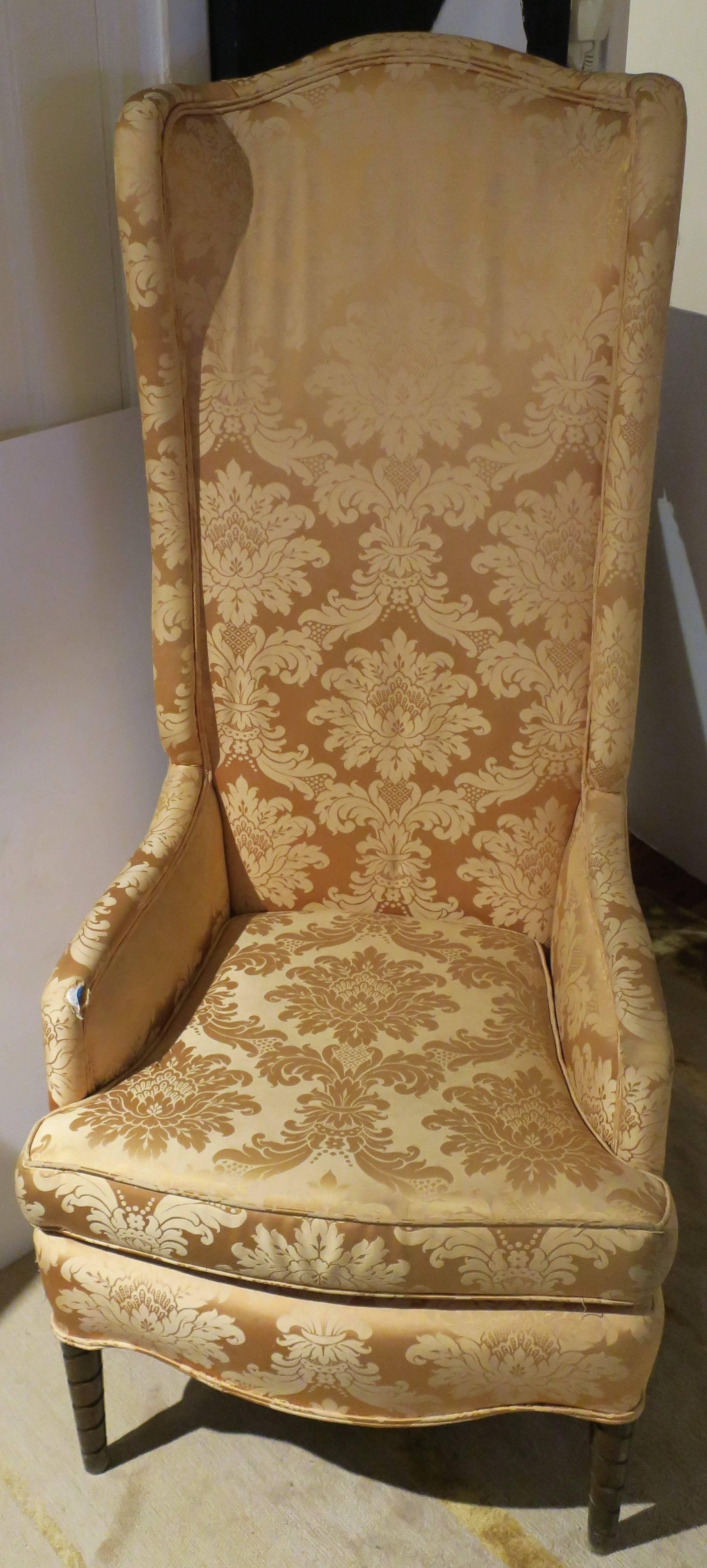 A well made mid-20th century tall back wingback upholstered chair in a yellow-gold damask fabric, circa 1960s. Measurements include: 56