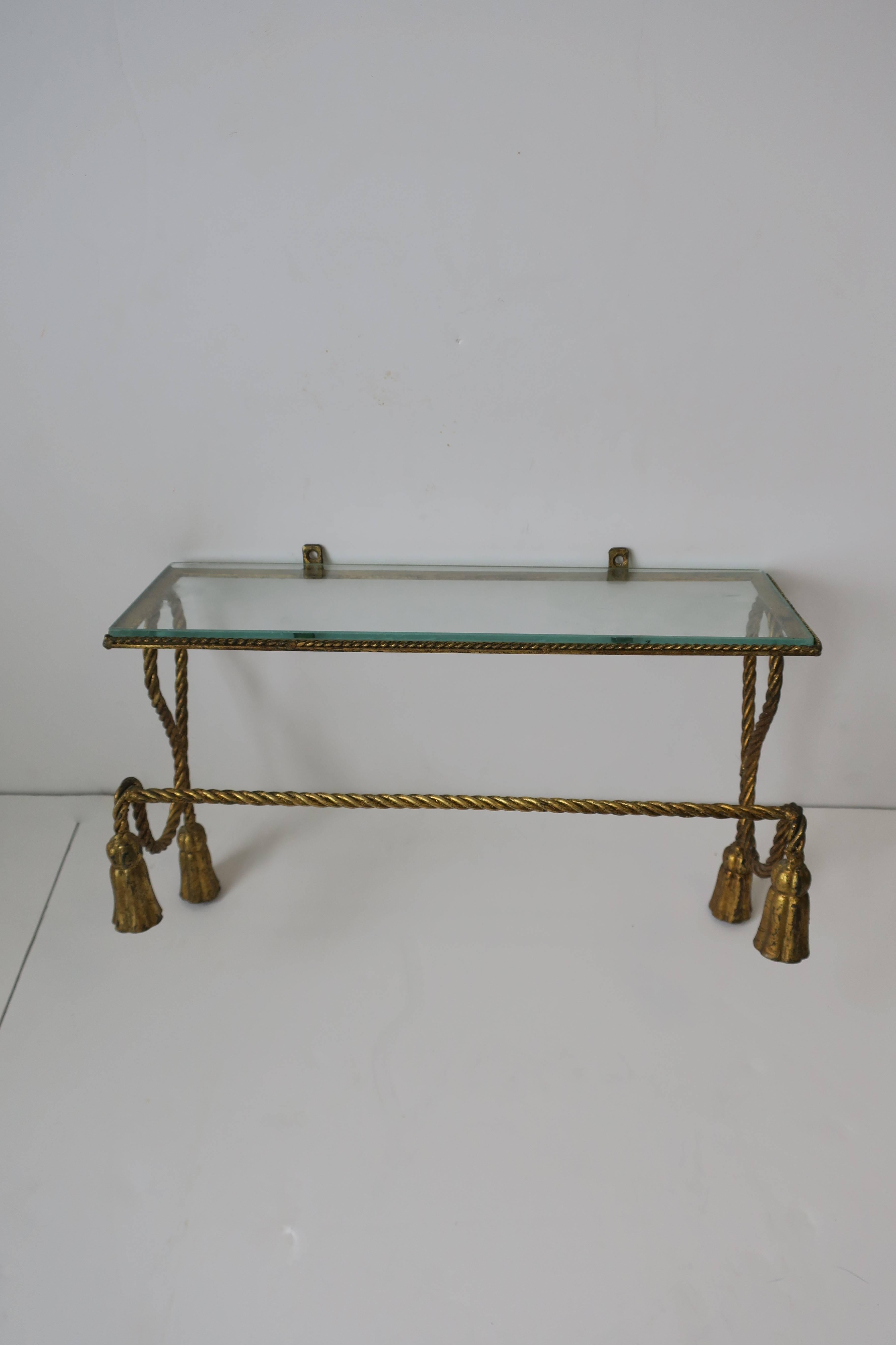 A beautiful Mid-Century Italian gold gilt tole metal and glass bathroom vanity wall shelf with decorative 'tassel' details at sides. Gold gilt tole metal frame with shelf also has a bar for face or hand towels.

Measurements include: 11.25 in. H x