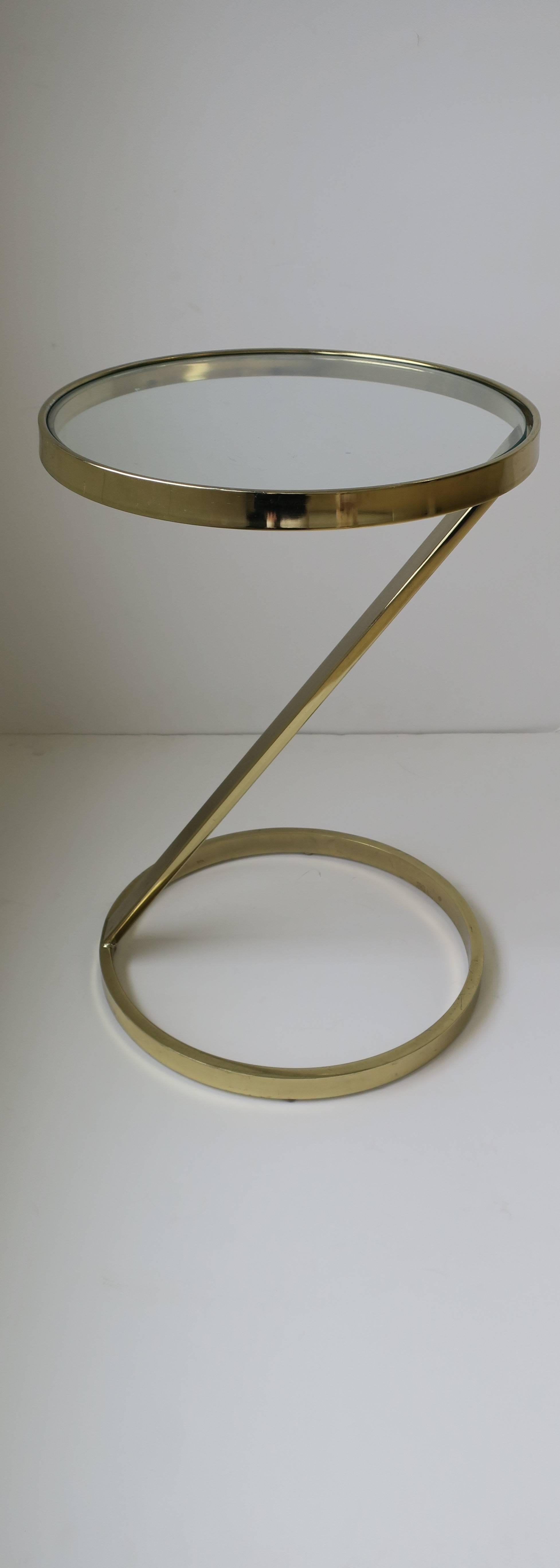 A Modern style round brass plated and glass side or drinks table in the style of designer Milo Baughman, circa Late 20th century. 

Table measures: 14.5