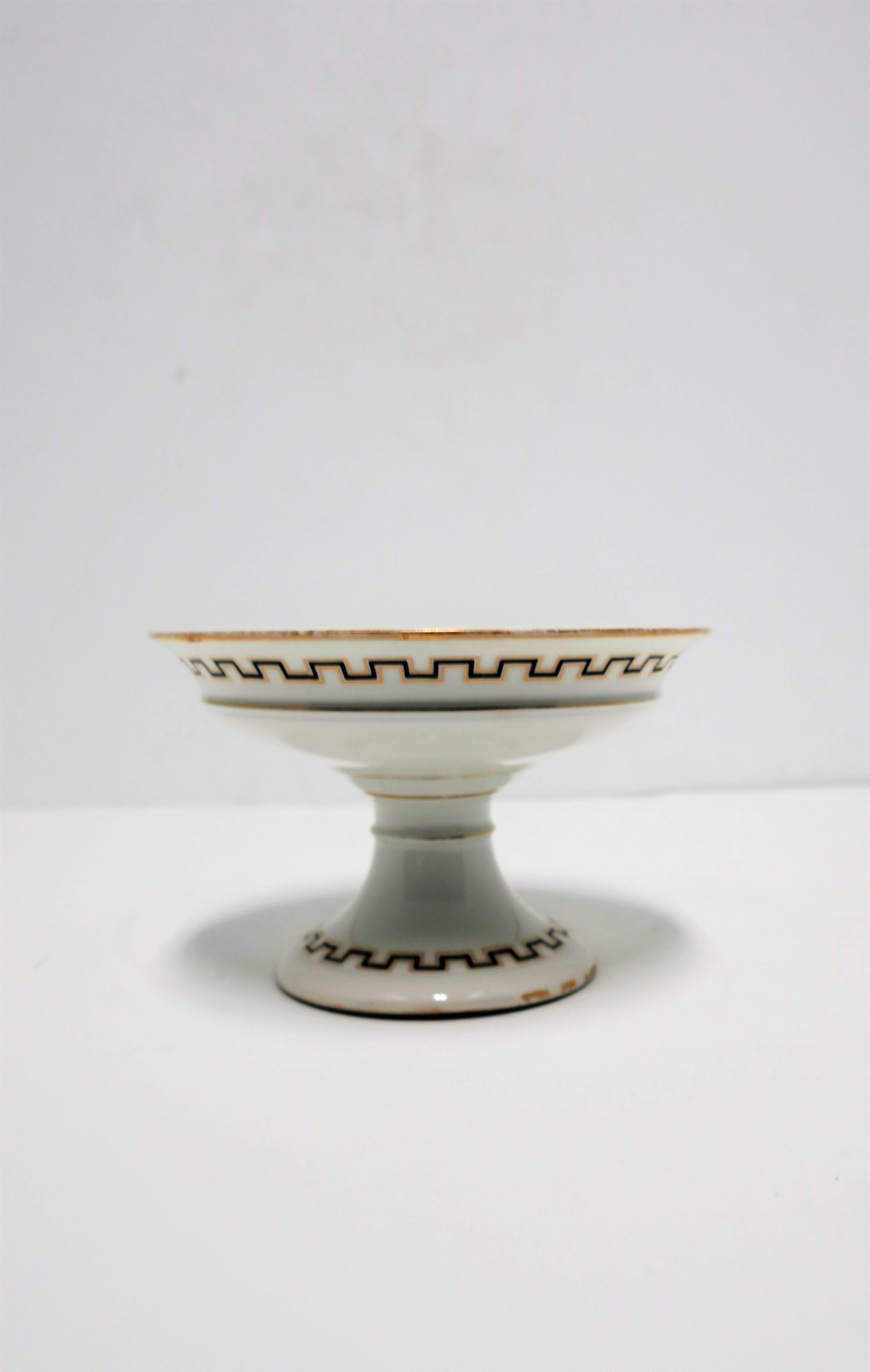 A beautiful Italian white, black, and gold ceramic tazza or compote footed pedestal bowl in the Greco-Roman or Classical Roman style, circa mid-20th century, Italy. Piece bears three heads or faces that surround interior area, accompanied by a
