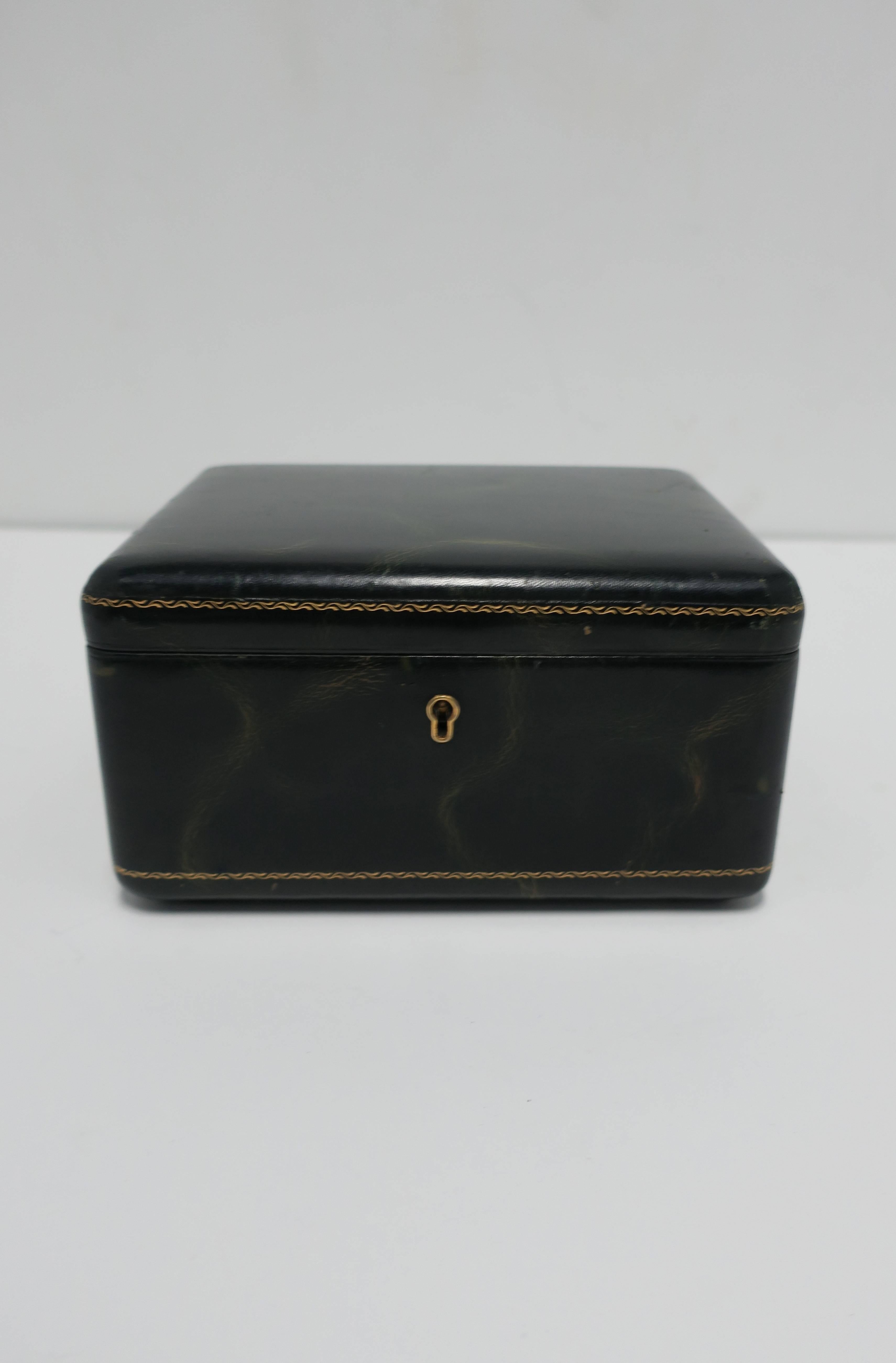 A beautiful Midcentury dark green leather jewelry box with removable tray. This dark green leather box has beautiful gold embossing around and brass keyhole detail on front. Inside, piece is upholstered in a gold/yellow material. Box is large enough