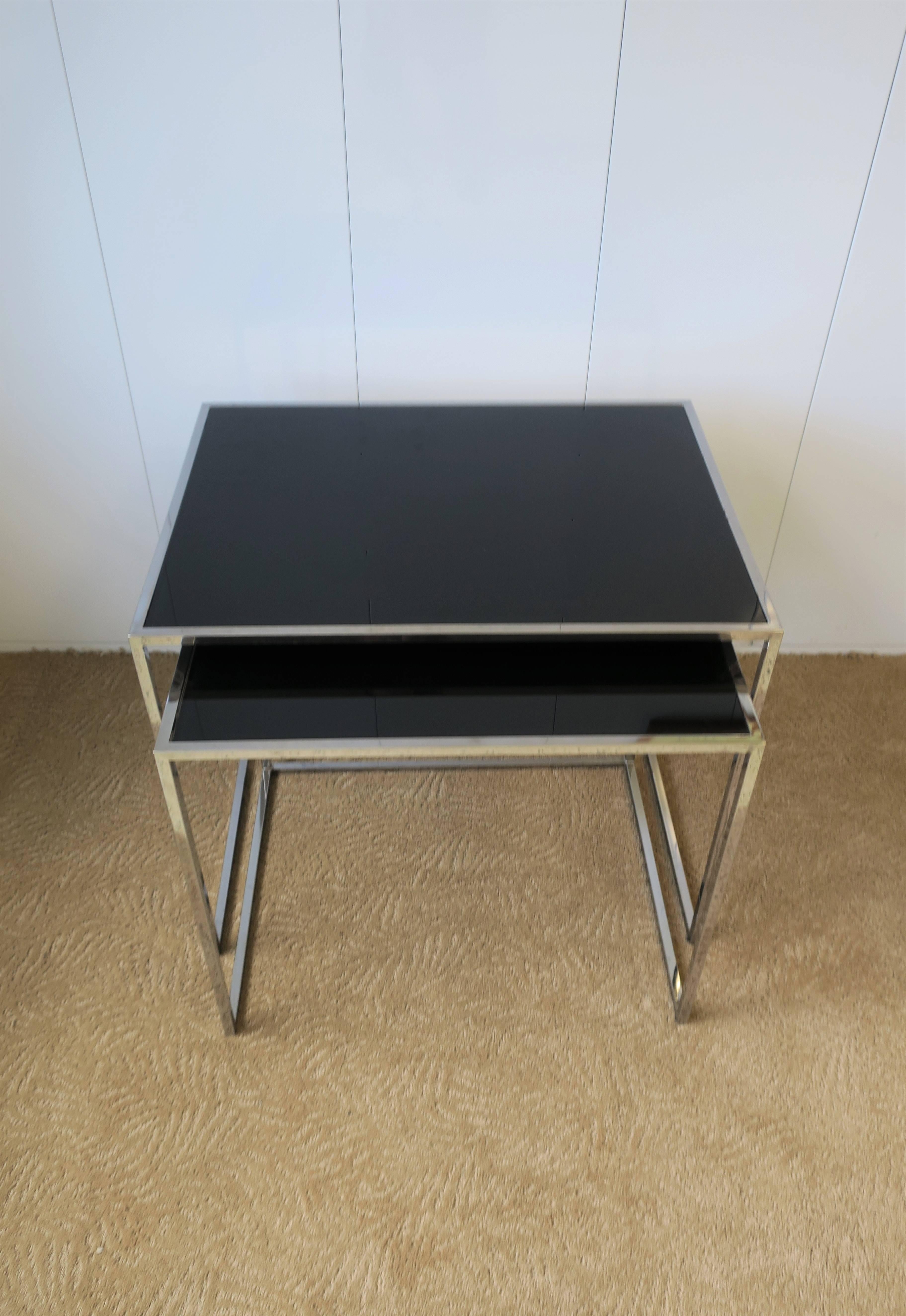 A vintage set of two minimalist chrome and black glass top nesting or end tables. 

Tables measure: 
19.75 in. H x 23.5 in. W x 17.75 in. D
18.25 in. H x 21 in. W x 16.50 in. D


