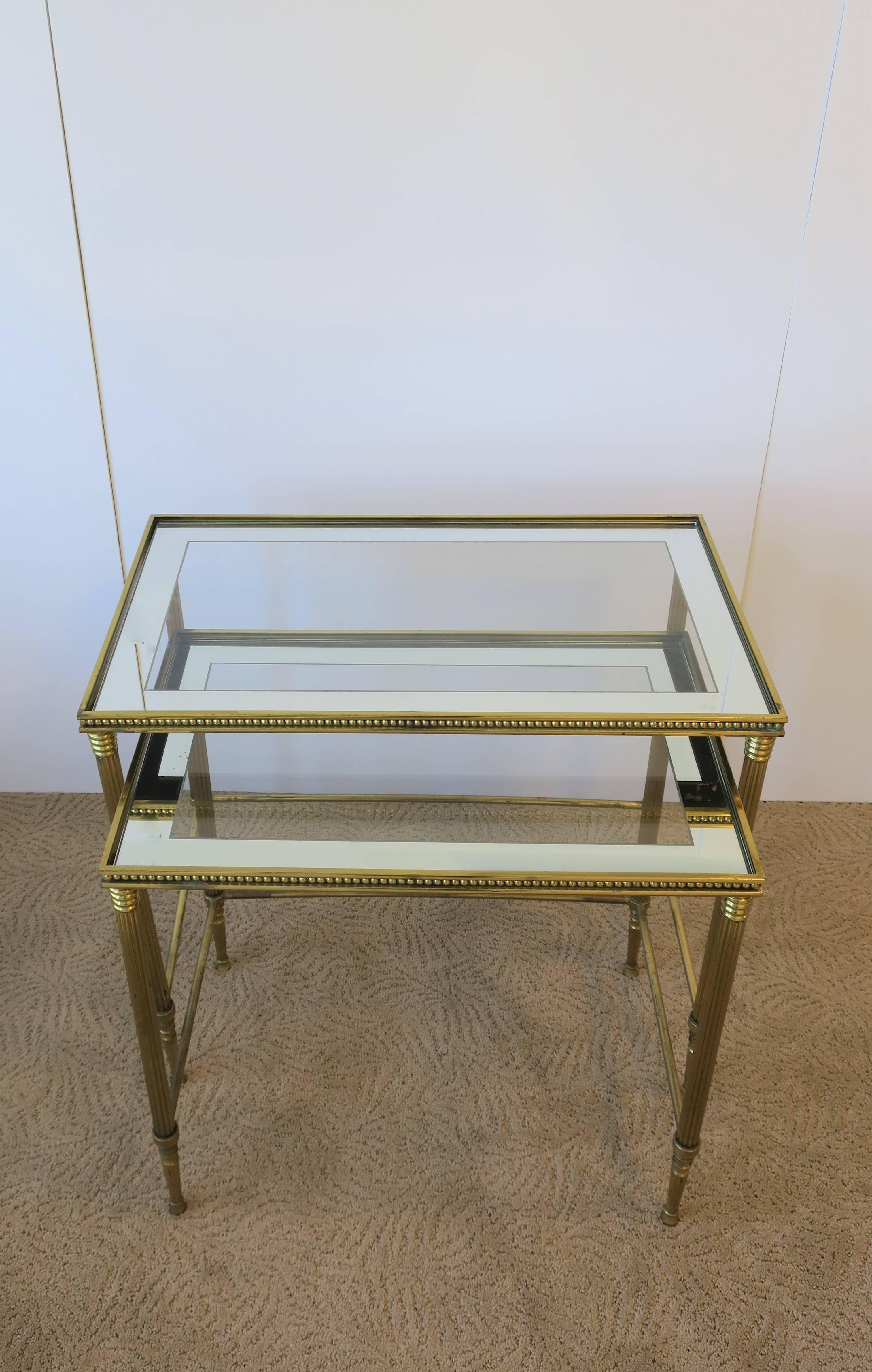 A vintage set of Neoclassical Italian brass and glass nesting tables or end tables, Italy, circa 1960. Glass top with mirrored edge. In the style of Maison Bagues. 

Measurements:
20.5 in. H x 23.25 in. W x 13.75 in. D
18.5 in. H x 20 in. W x 13
