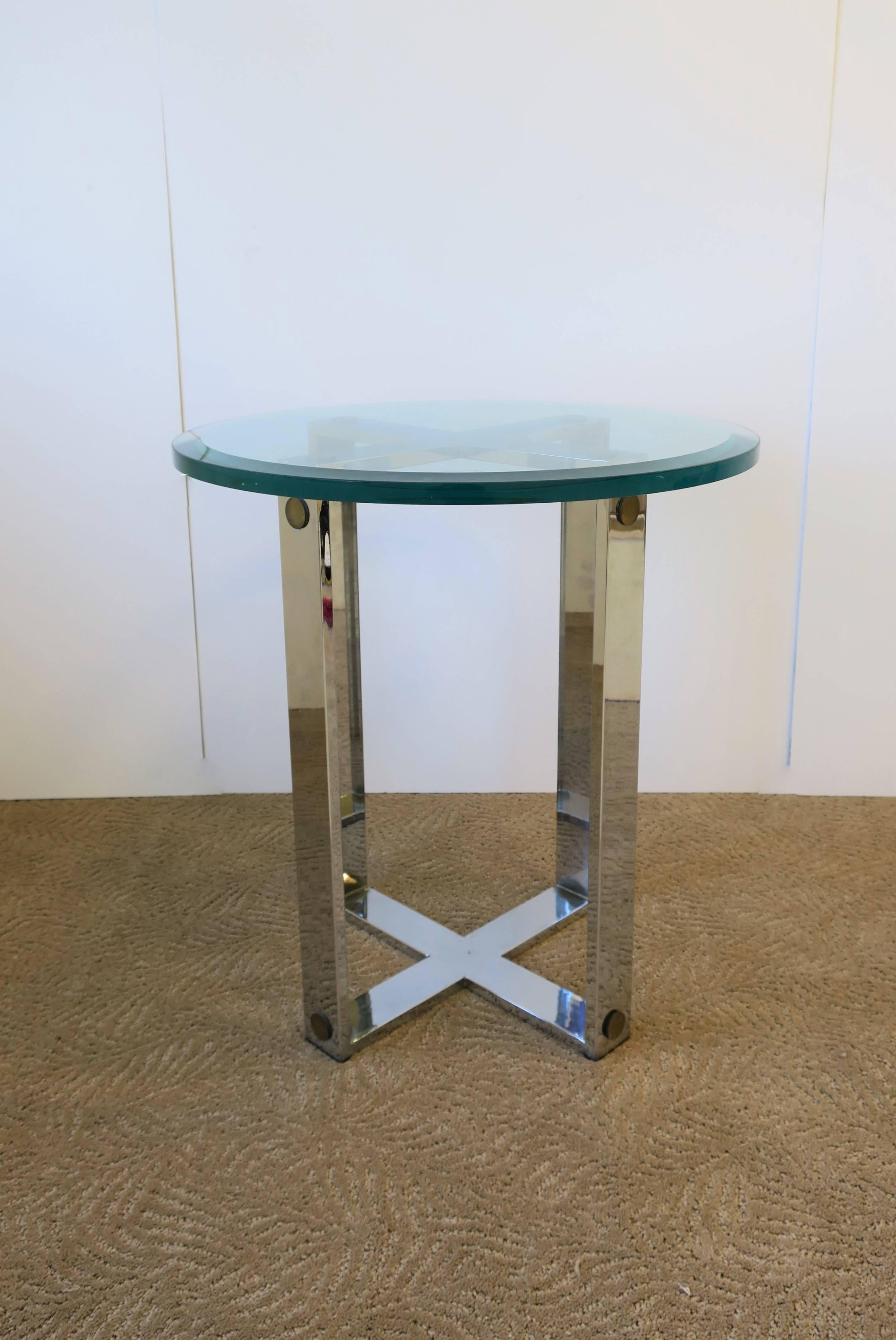 A vintage chrome, brass, and glass round end or side table in an Art Deco style, circa late 20th century. Substantial chrome frame/base with round geometric brass accents, finished with a significant round glass top measuring over 1 in. high at .63