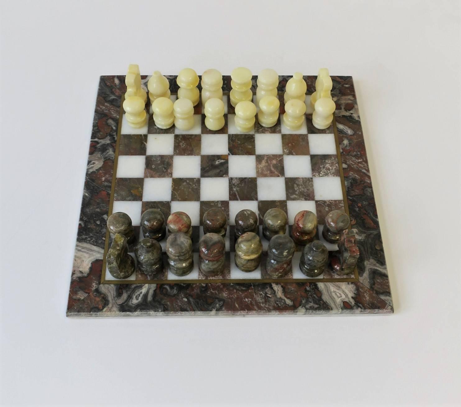 A marble and brass chess game set, ca. 1970s. Marble game board has a beautiful brass inlaid trim and marble colors that include: white and a marble combo of white/blue/grey and red/burgundy/ox blood hues. 'White' game pieces are lacquered alabaster
