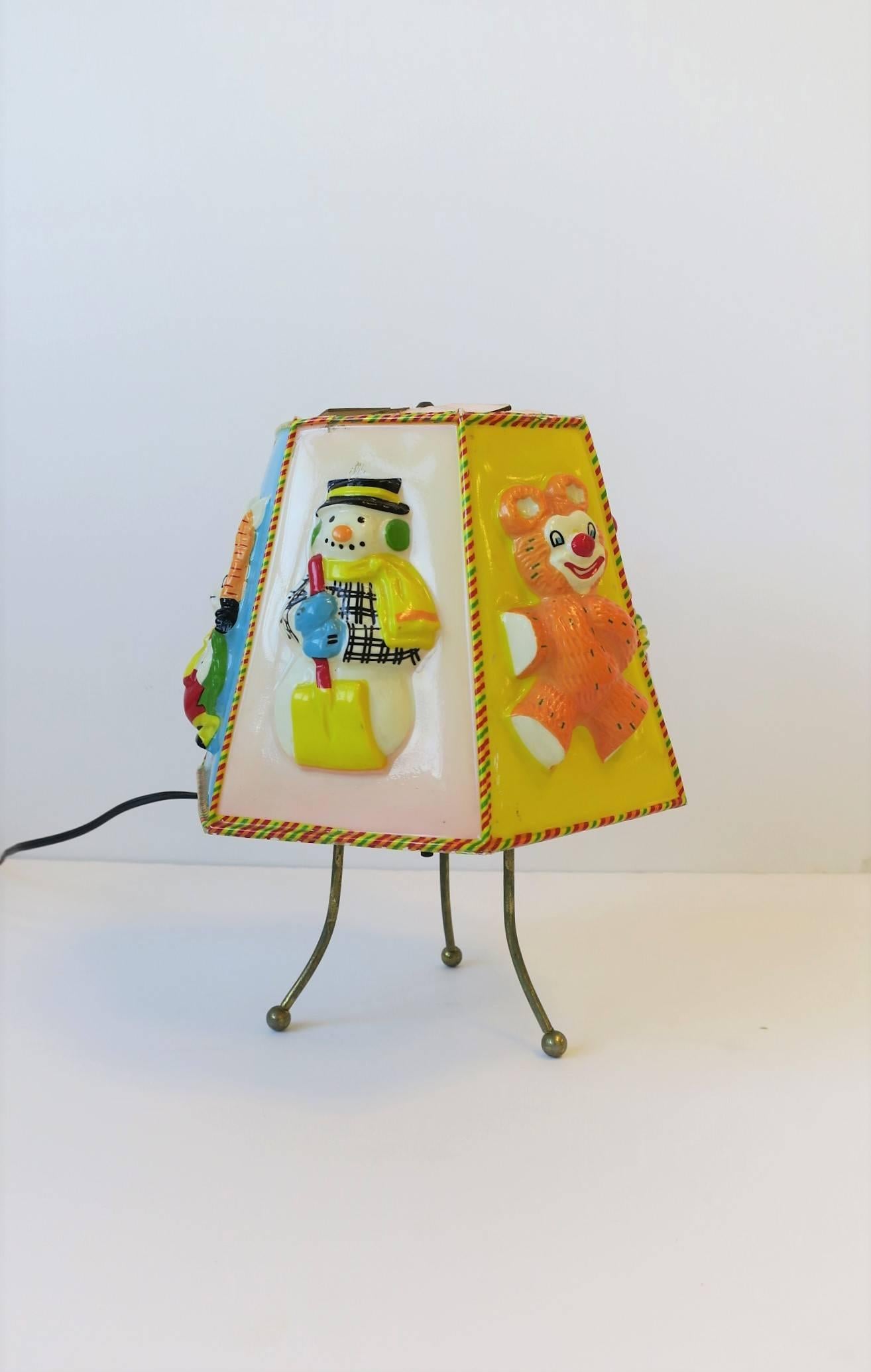 A fun rare vintage baby or child's table lamp with brass tri-pod base, circa Mid-20th century, 1960s. When light is 'on' lampshade rotates 360 degrees using the warmth of the lightbulb. Lampshade features fun figures and animals. 

Lamp measures: 8