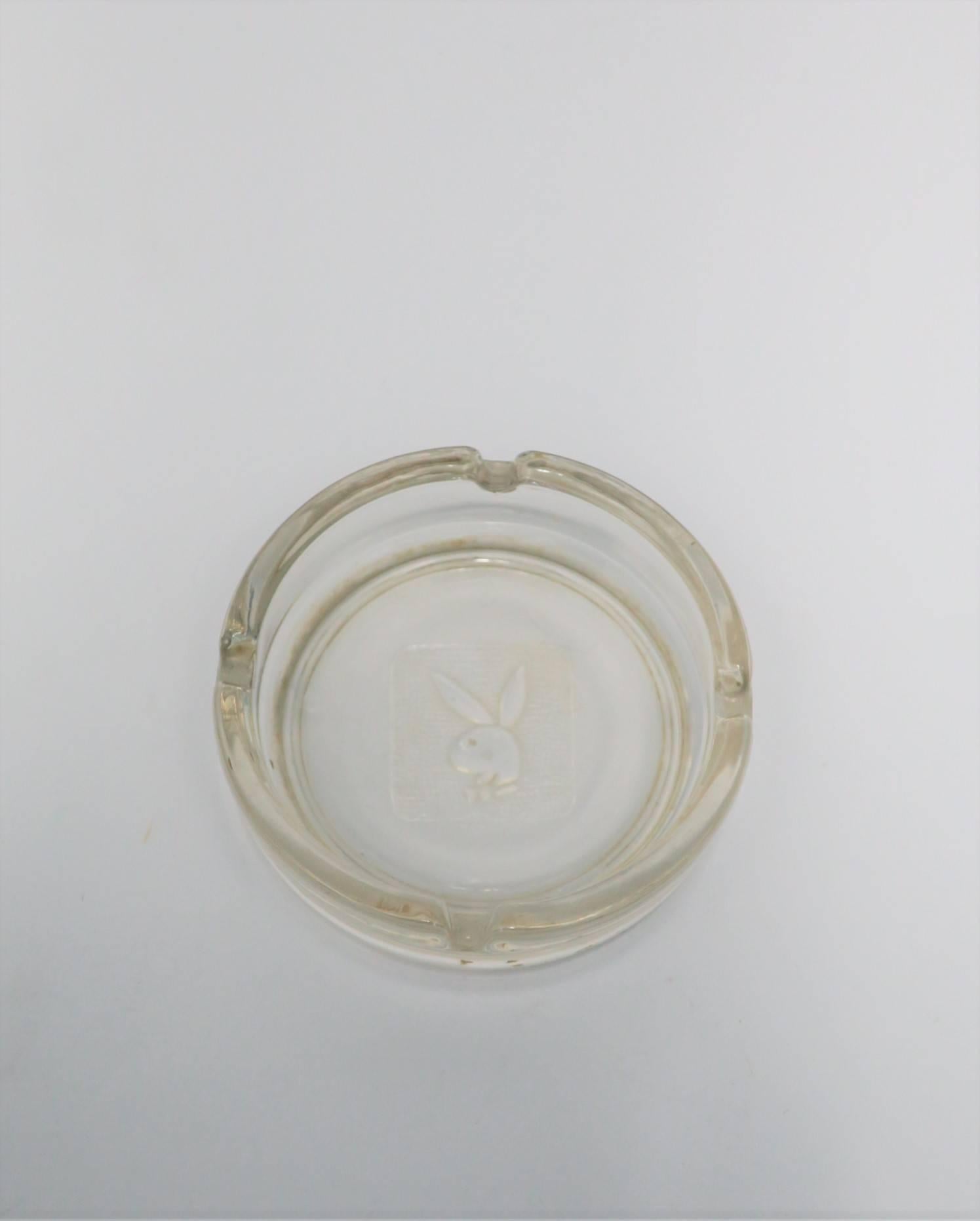 A vintage Playboy glass ashtray, circa 1970s Playboy Club New York. Glass ashtray has embossed iconic 'Playboy' bunny. Four indents around rim. In addition to it's function as an ashtray, piece can also be used as a standalone decorative object,