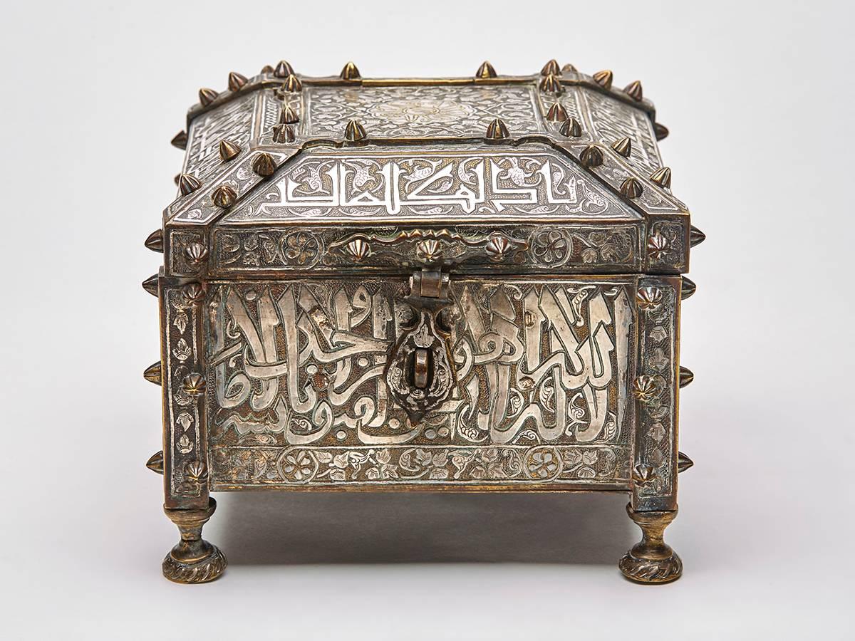 An exceptional antique Islamic holy casket with Arabic text, probably from the Koran with inlaid silver, gold, brass and copper and with a very Fine inlaid wood and mother-of-pearl parquetry interior. The square shaped box stands raised on four feet