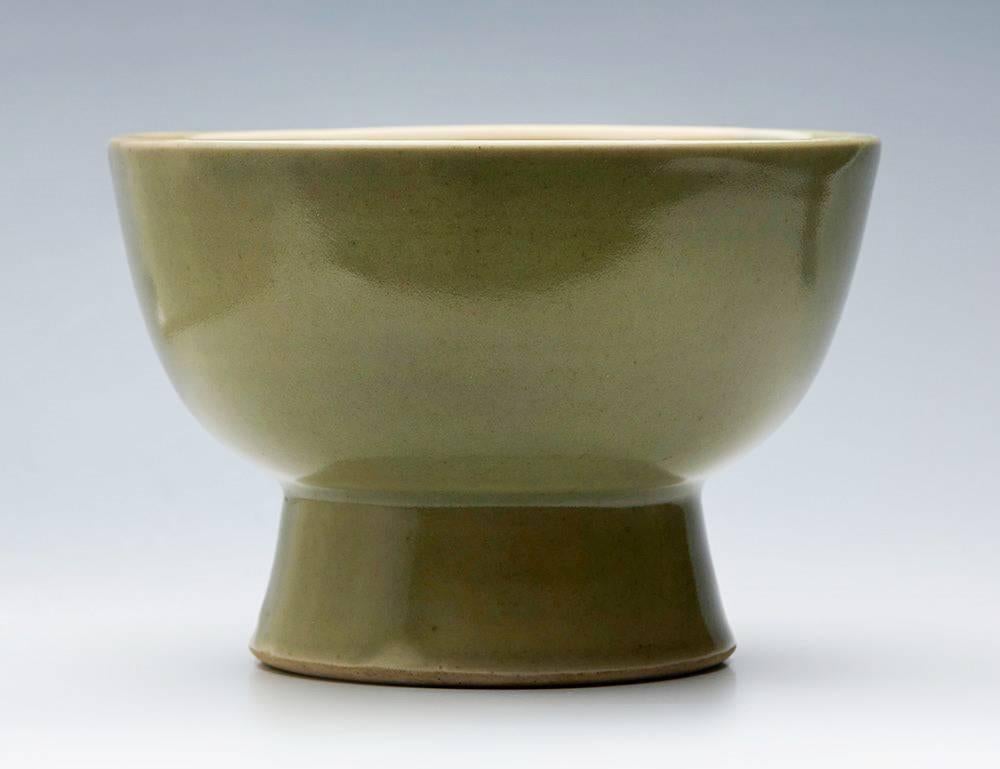 A Leach Pottery studio pottery footed bowl decorated in celadon glazes by David Leach and dating from the early to mid-20th century. The rounded porcelain bowl stands raised on a conical shaped foot and is decorated in celadon green glazes with a