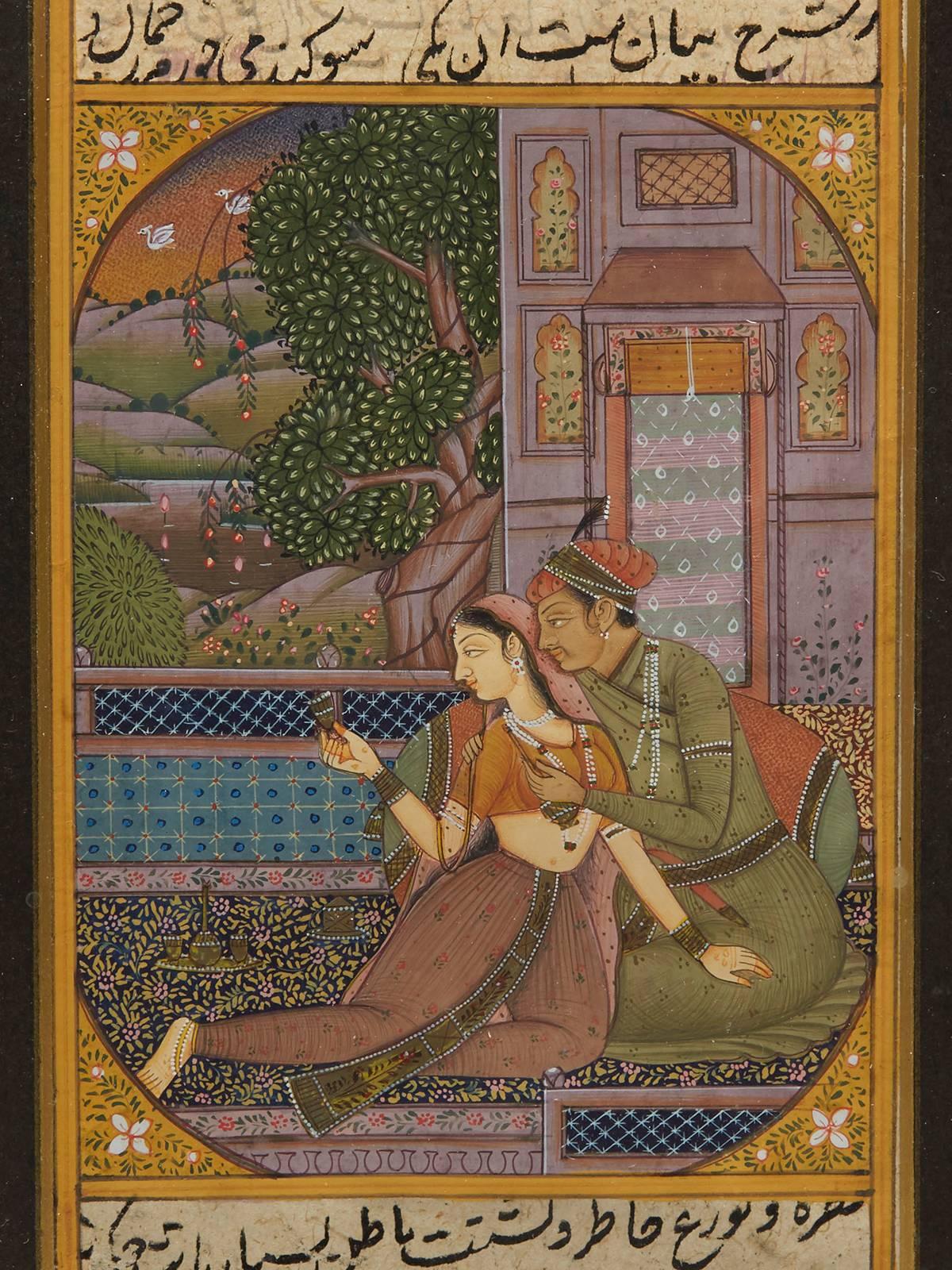 A fine antique framed Mughal illustrated leaf from a manuscript with a scene of lovers drinking and seated on a carpet next to a window opening to a landscape scene. The manuscript has black calligraphy to the front and back and has been mounted