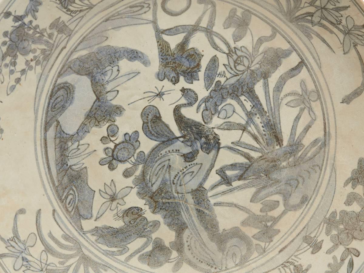A large Chinese dish of rounded shape with a raised rim hand-painted in underglaze blue with birds and an insect in a pond with flowering blooms set within a floral and bird painted border with painted designs to the underside of the dish. The base