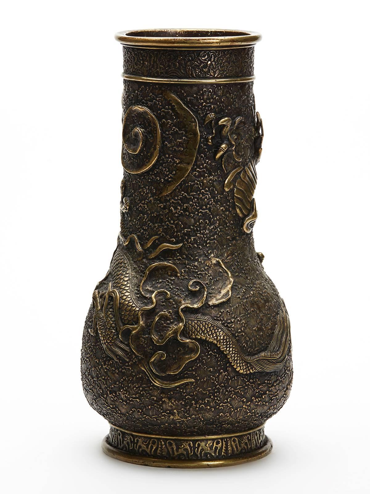 A large and impressive antique Japanese Meiji bronze vase moulded in relief with a scrolling dragon amidst clouds on a fine patterned and textured ground with decorative borders around the top and foot of the vase. The vase has a rounded bulbous