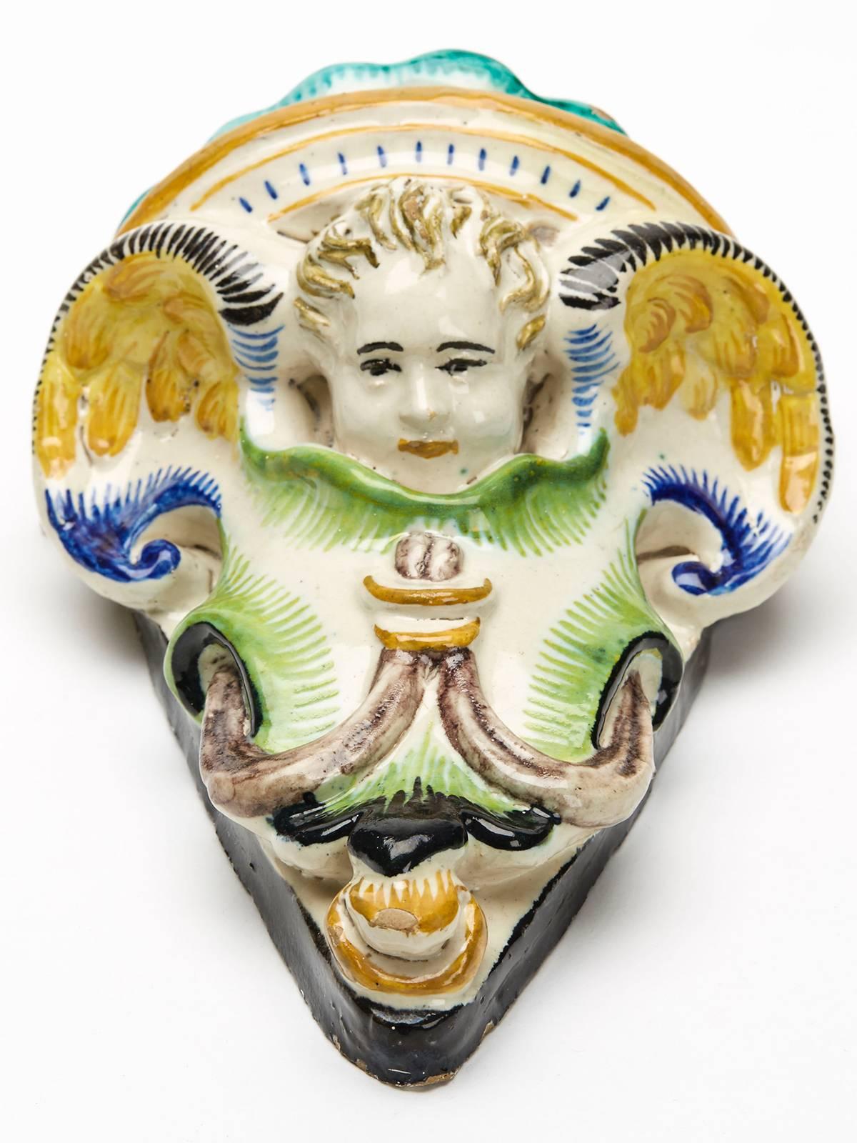 A stunning and rare antique Italian Cantagalli Maiolica pottery wall pocket moulded with a winged cherub set within a scroll design surround with hanging tassels. The pocket is hand-painted in coloured enamels on a cream coloured ground with a black