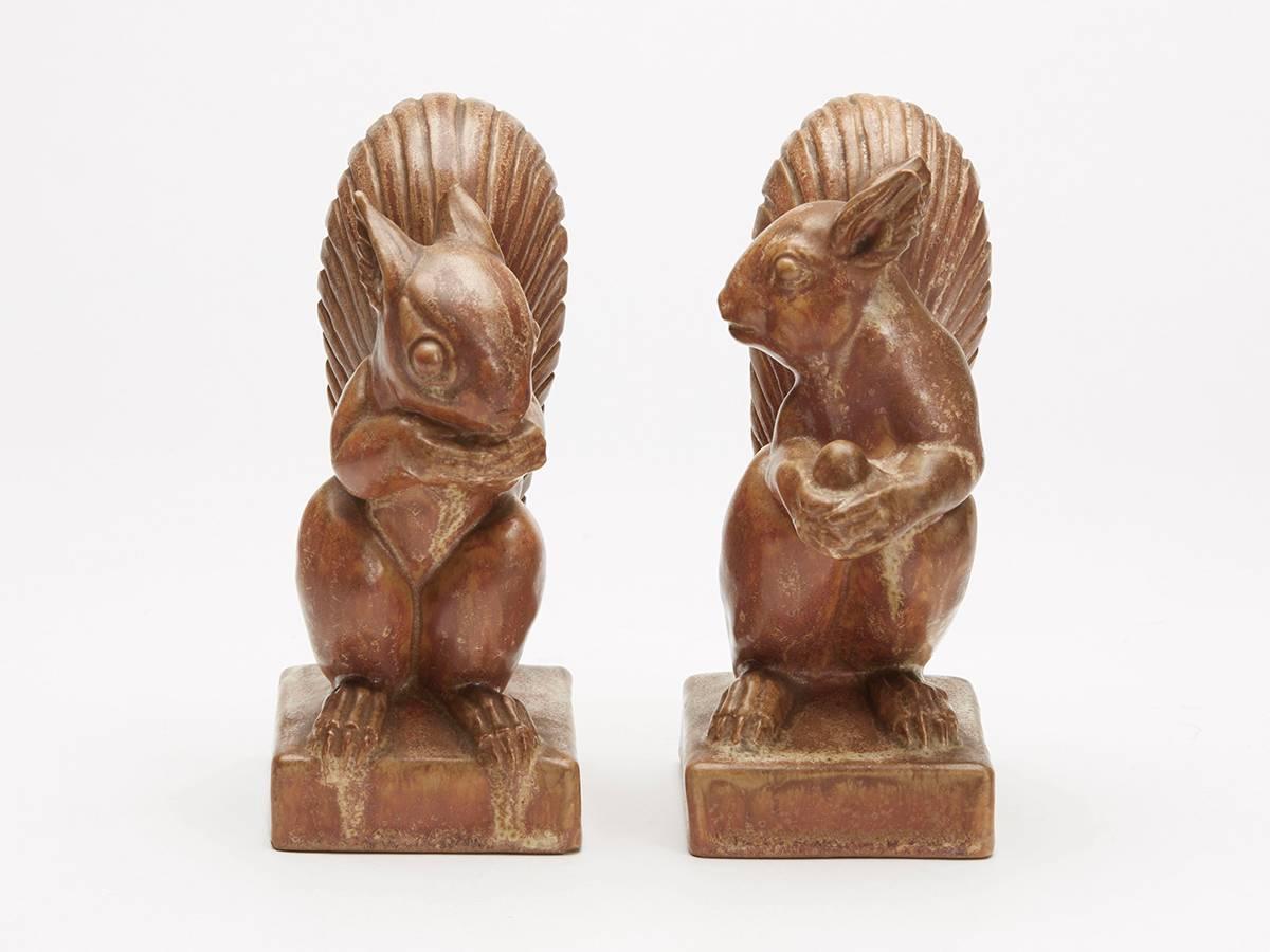 A rare pair Doulton Lambeth art pottery squirrel bookends designed by Florrie Jones. The stoneware squirrels stand on a rectangular base one holding a nut in front of him and looking sideways while the other eats a nut. The squirrels are decorated