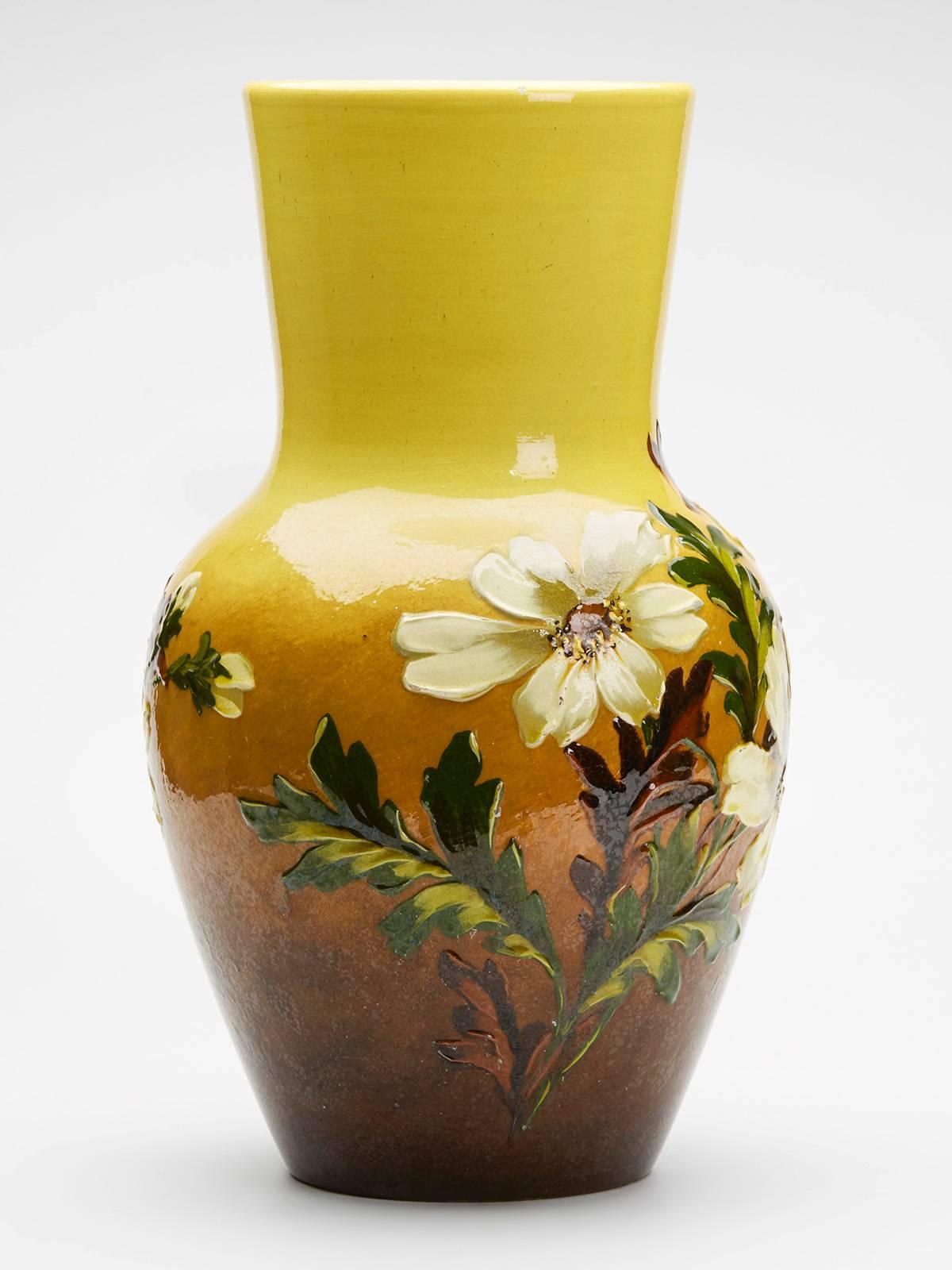 A large Arts & Crafts Burmantofts art pottery faience vase richly painted in thick glazes with floral designs on a graduating yellow and brown ground. The earthenware baluster vase has a wide funnel shaped top with a slight trumpet shape and the
