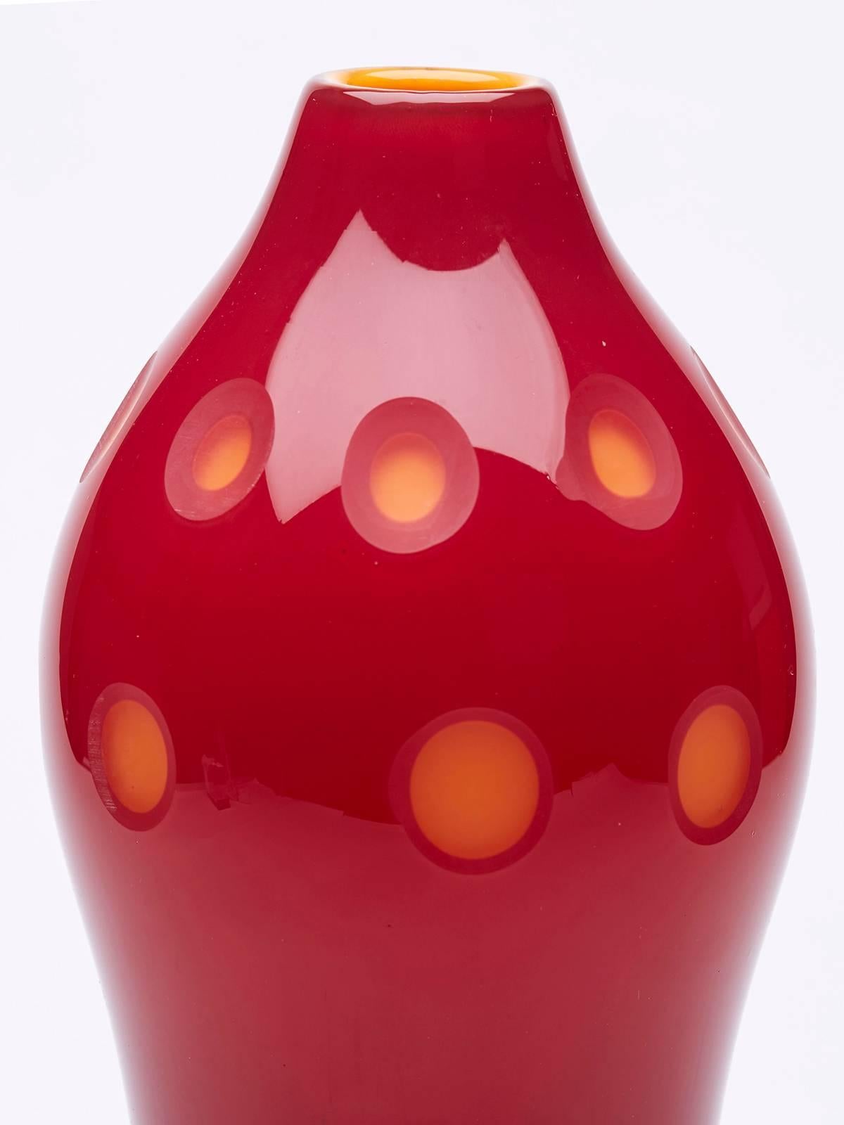 A stunning and unusual vintage Italian Venini, Murano red cased art glass vase with slice cut window designs. The bulbous shaped vase is cased in red over clear glass with an orange cased inner. The colour graduates from a brown colour around the