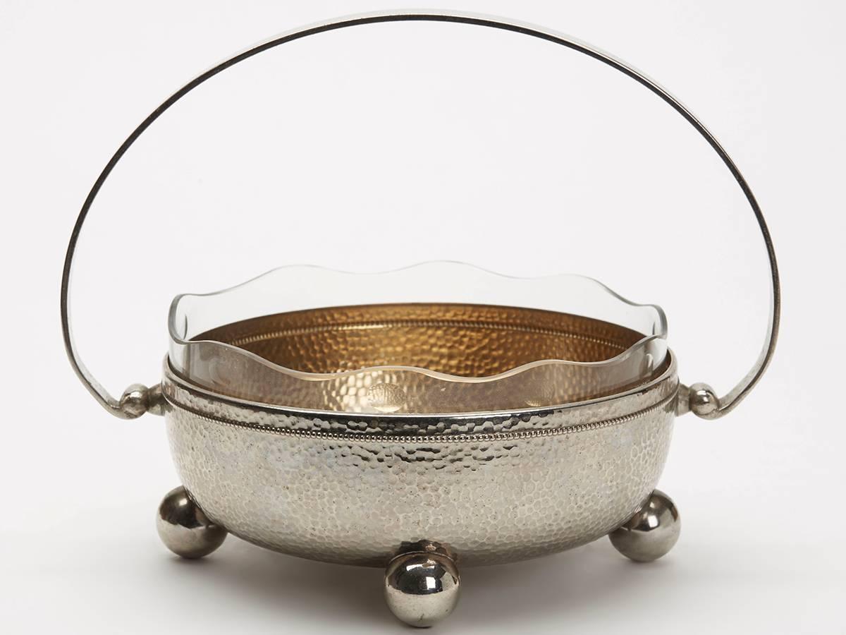An Art Nouveau German WMF Wurttembergische Metallwarenfabrik handled silver plated bowl with original glass liner. The rounded silver plated bowl stands raised on four large ball feet with a flat strap raised handle attached to either side. The bowl