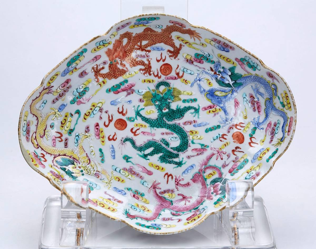 A stunning antique Chinese porcelain pedestal bowl or dish finely decorated with five various coloured scrolling dragons chasing flaming pearls amidst clouds within the dish, four further dragons in similar pursuit below the edge and with a painted