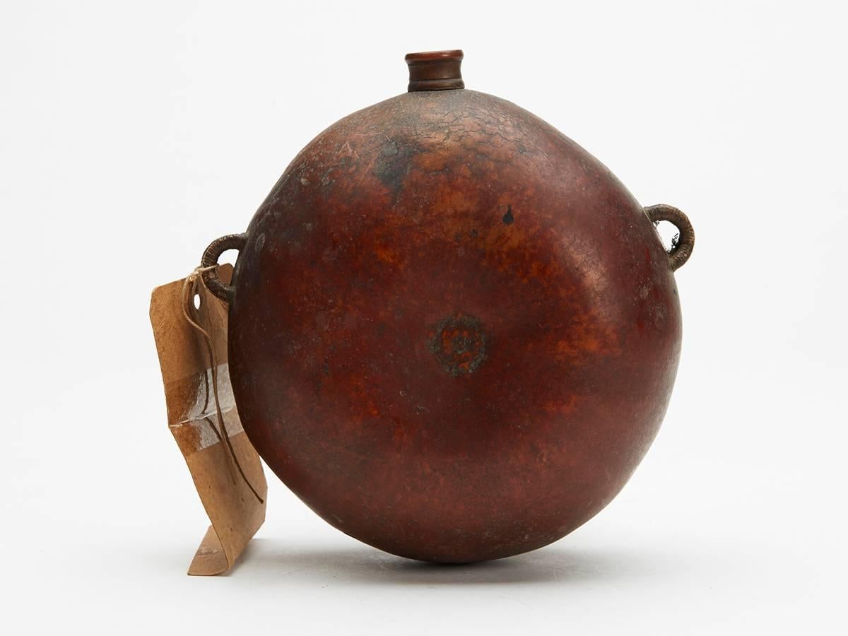 A fine antique African gourd water bottle with woven carrying handles applied to the sides and with a carved wooden pourer inserted into the top rim. The gourd has a wonderful age patination and is not marked. It comes with provenance with an old