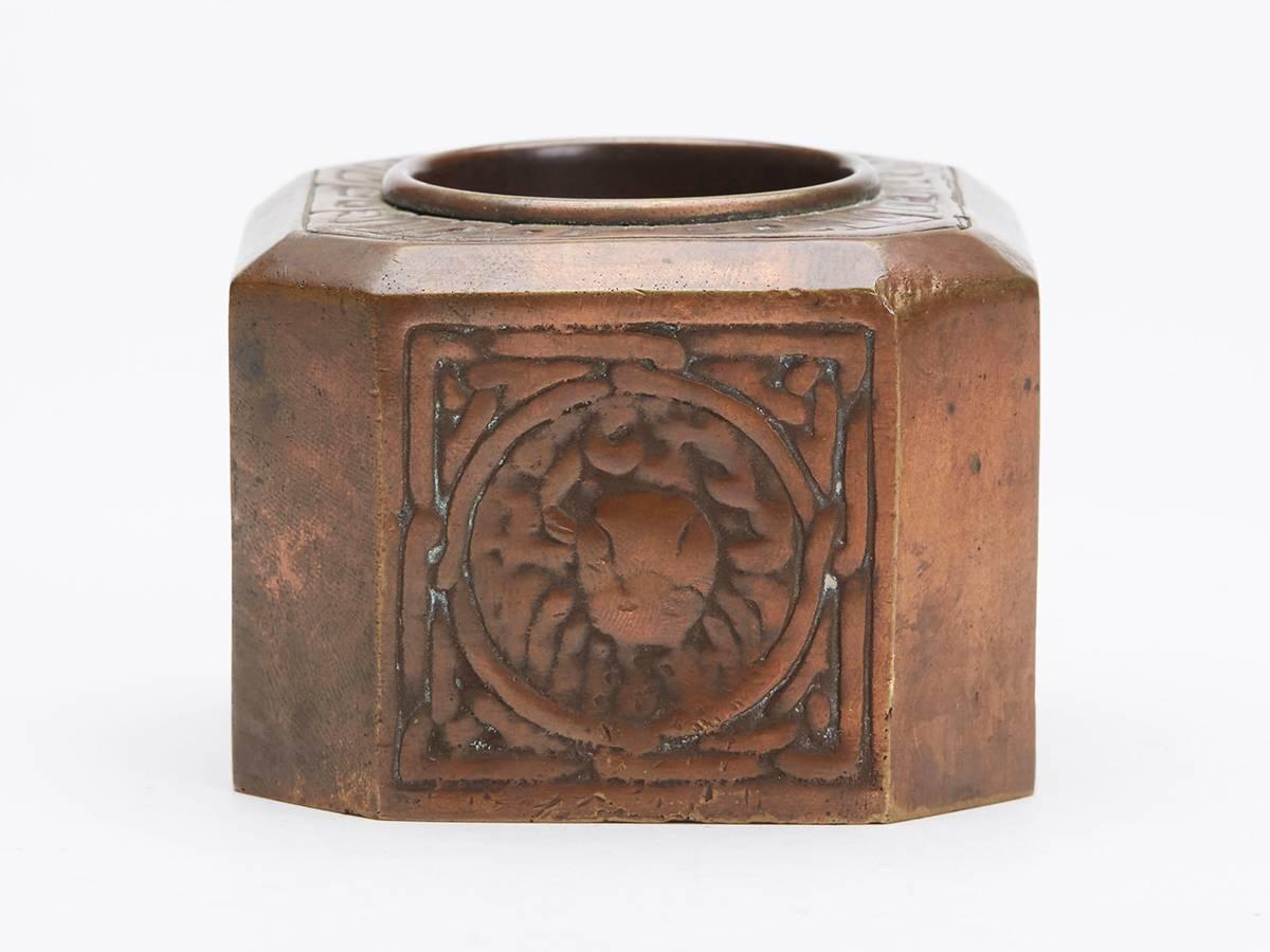 A Tiffany studios bronze zodiac pattern inkwell of square shape with angled corners with four sides moulded with rounded panels containing signs from the zodiac. The heavily made inkwell has a central top recess within a decorative border and the