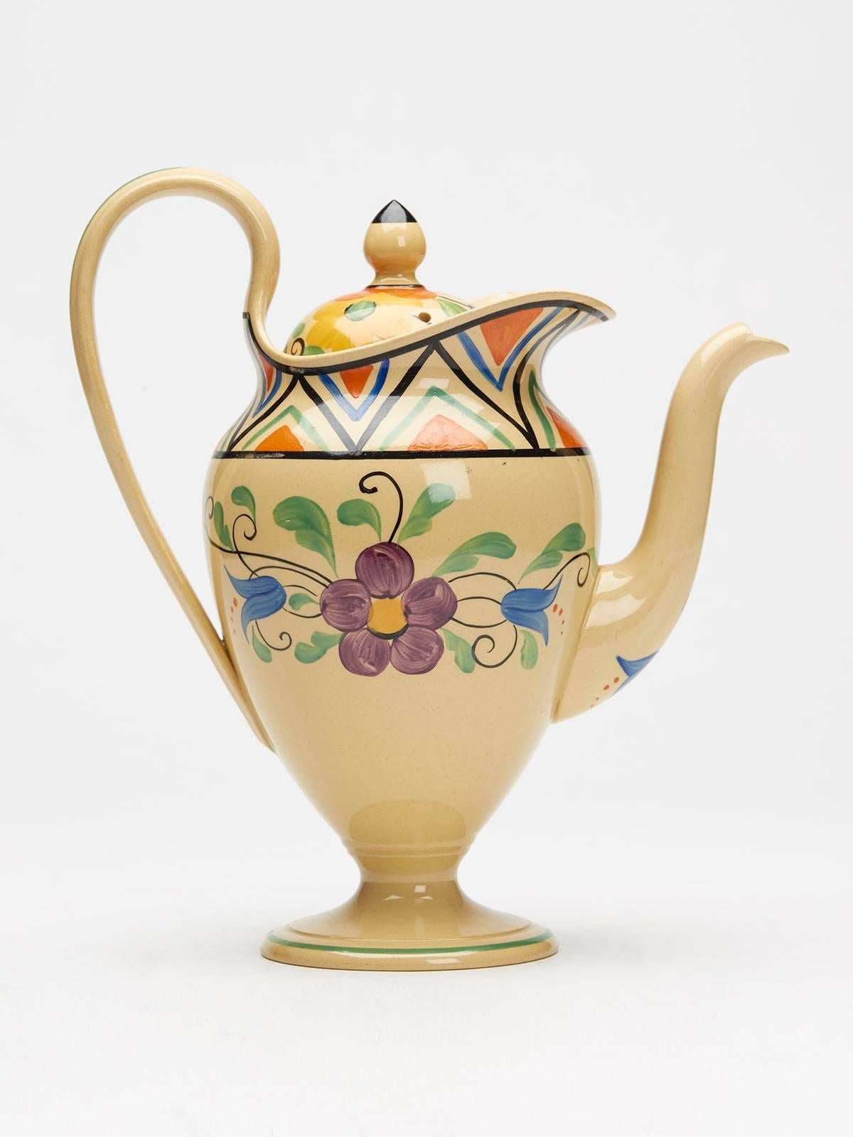 An Art Deco Wedgwood floral coffee pot and cover by Millicent (Milly) Taplin hand painted in brightly colored enamels with floral and geometrical designs on a drab (cane) colored body. This elegantly shaped coffee pot standing on a pedestal foot has