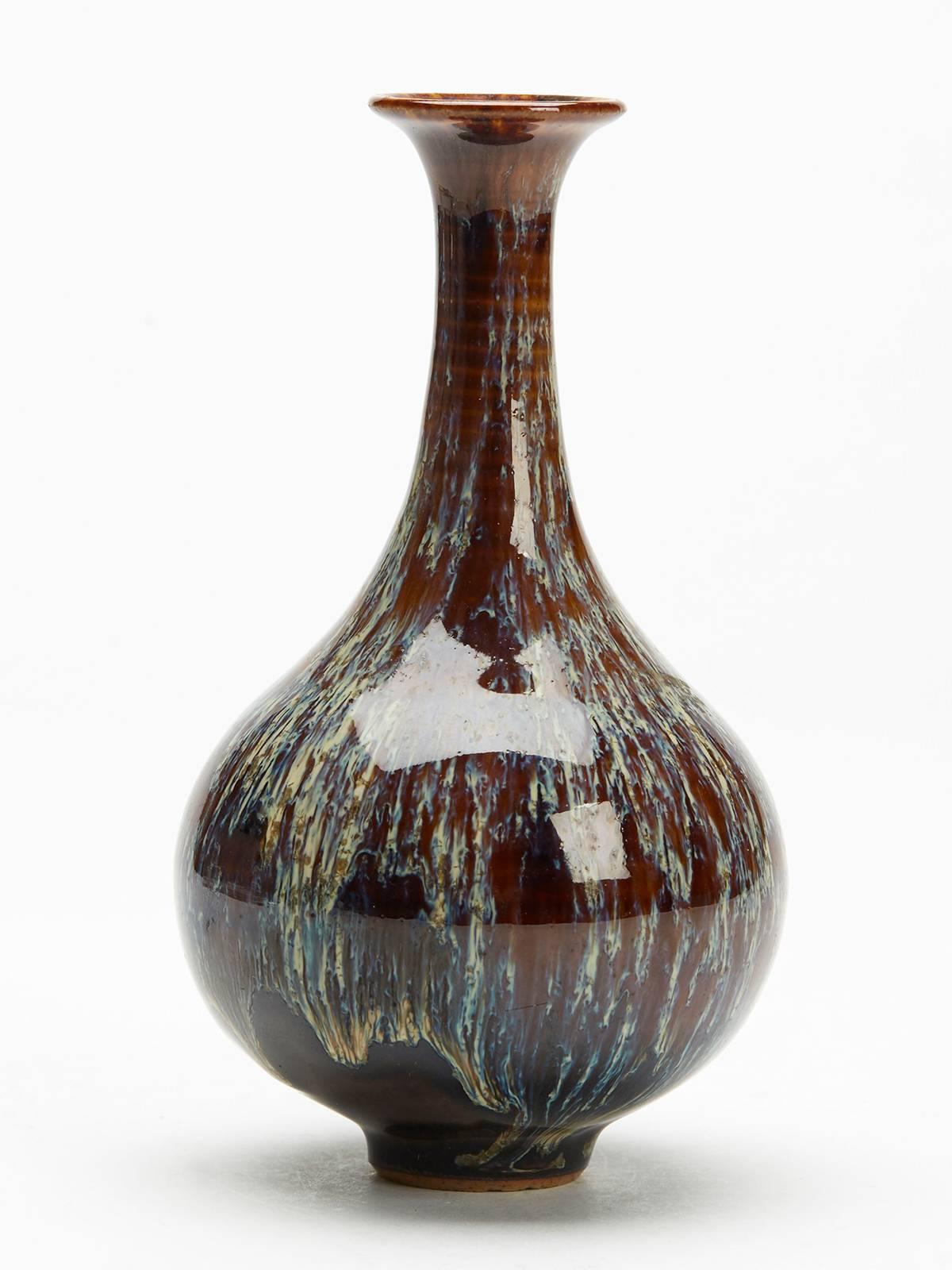 A hand thrown antique Chinese bottle vase decorated in Junyao glazes dripped over a brown glazed ground and dating from the 19th or early 20th century. This finely made vase stands on a narrow rounded unglazed foot and has a rounded bulbous body and