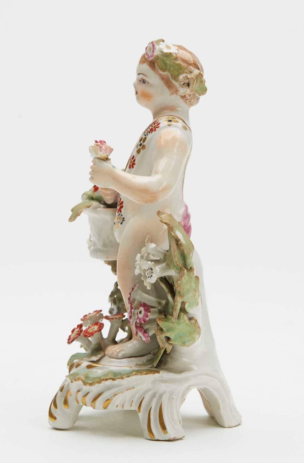 As part of a fine collection of early English porcelain, we offer this rare antique bow figure of a putti carrying a basket of fruit and dating from circa 1765. The figure stands raised on a scroll work base heightened with gilding and stands