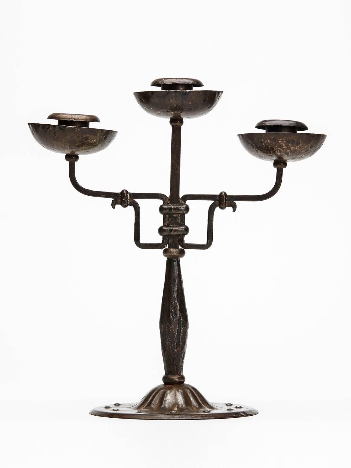 A stylish Austrian secessionist Industrial art patinated steel triple candlestick by Hugo bergere. The candlestick stands on a wide rounded foot with box steel arms with a raised central candle holder within a rounded cup drip tray with similar