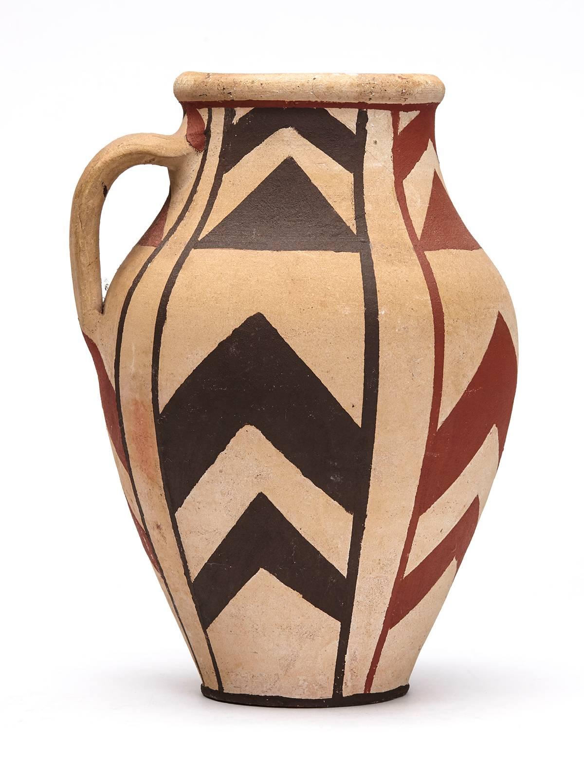An unusual Studio pottery handled vase (or possibly a jug) hand-painted with native style decoration on an unglazed ground. The large bulbous earthenware vase is hand thrown with a small handle to the top rim and is hand-painted in red and black
