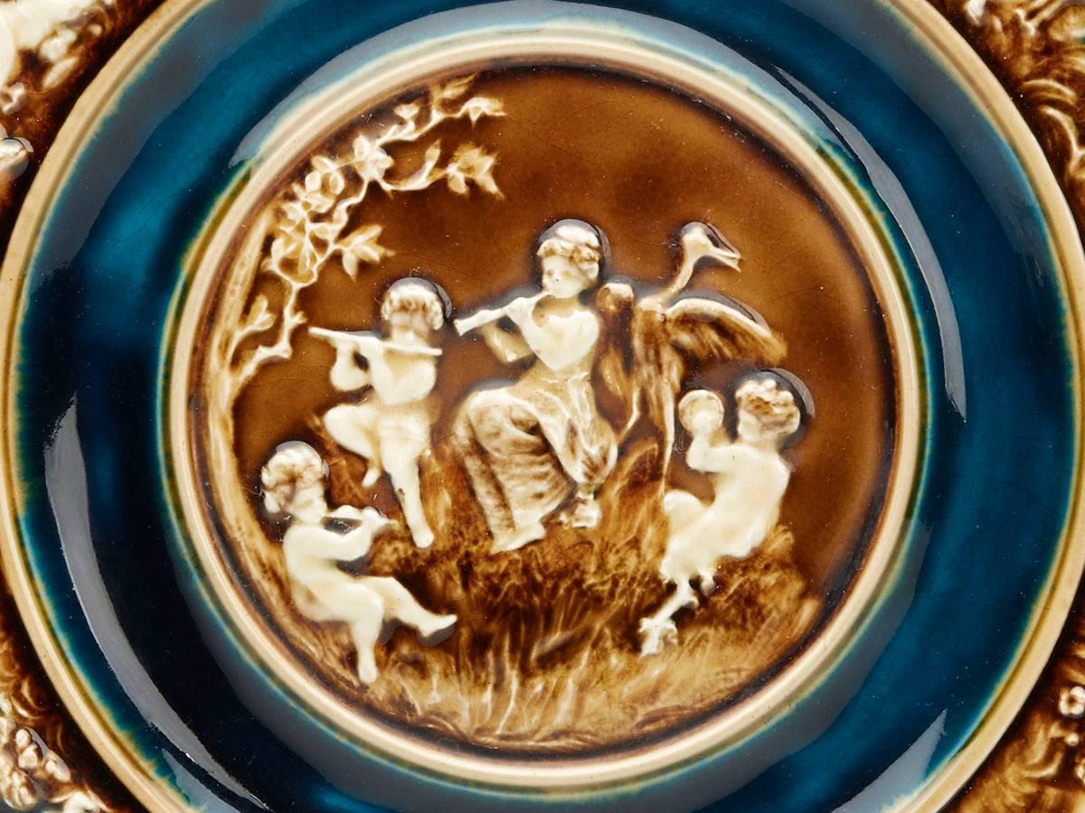 A fine antique Austrian Majolica charger moulded with a central classical figural scene with musicians within a landscape within a border of winged putti involved in various activity with some also playing instruments. The plate is painted in tones