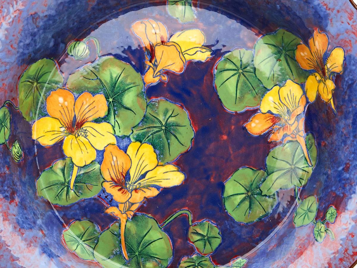 Eine alte Royal Doulton-Keramikschüssel mit Kapuzinerkresse-Muster:: gemalt in leuchtenden Farben auf einem blau-rot gesprenkelten Grund. Die breite:: flache Schale hat einen erhöhten und geformten Rand:: dessen Mitte mit leuchtend gelben