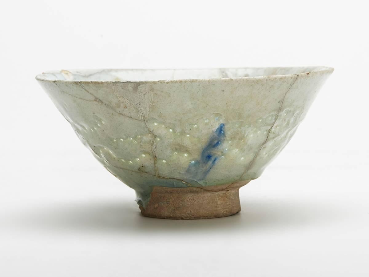 A rare Islamic earthenware bowl rounded conical form standing on a narrow rounded unglazed foot decorated in celadon glazes with blue streaked designs and with incised and pierced patterns around the rim, the piercing filled with glaze. The bowl is
