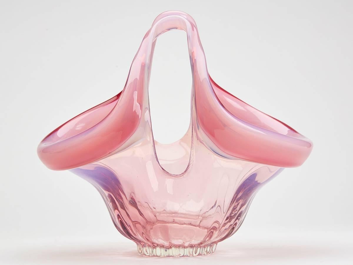 A fine and stylish vintage Italian Murano art twin handled glass basket hand blow in pink opalescent glass with pulled raised loop handles touching in the centre. The basket of oval shape stands on a narrow rounded foot with polished pontil and has