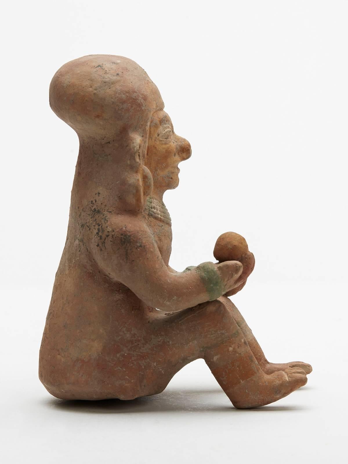 A fine Mexican Pre Columbian Jamacoaque seated pottery figure wearing a beaded necklet and wrist band and offering a ball in his right hand. The figure is made in terracotta colored clay with remnants of painted detail.

Provenance: Acquired by