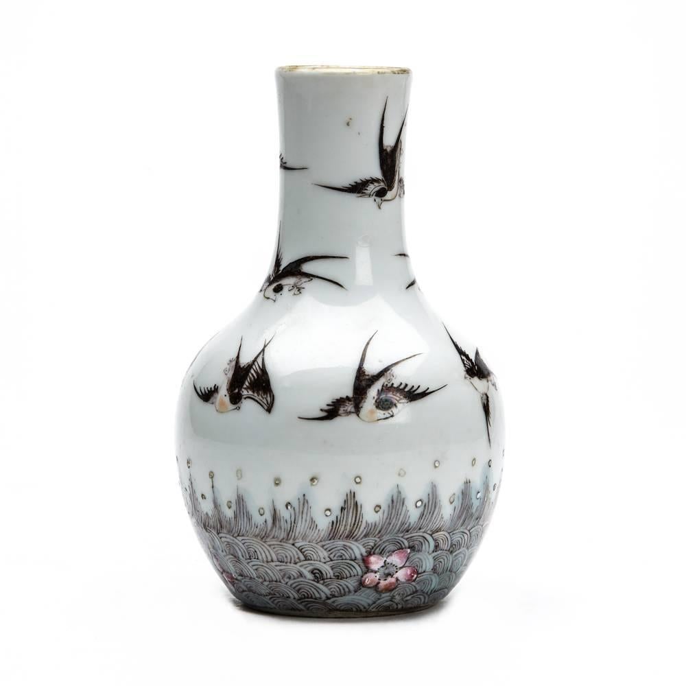 A fine and unusual antique Chinese Qing porcelain vase of bottle shape decorated with ten swallows flying above fields of grass with small flowering shrubs. The vase is well decorated on a white ground with an unglazed foot and gilded top rim and is