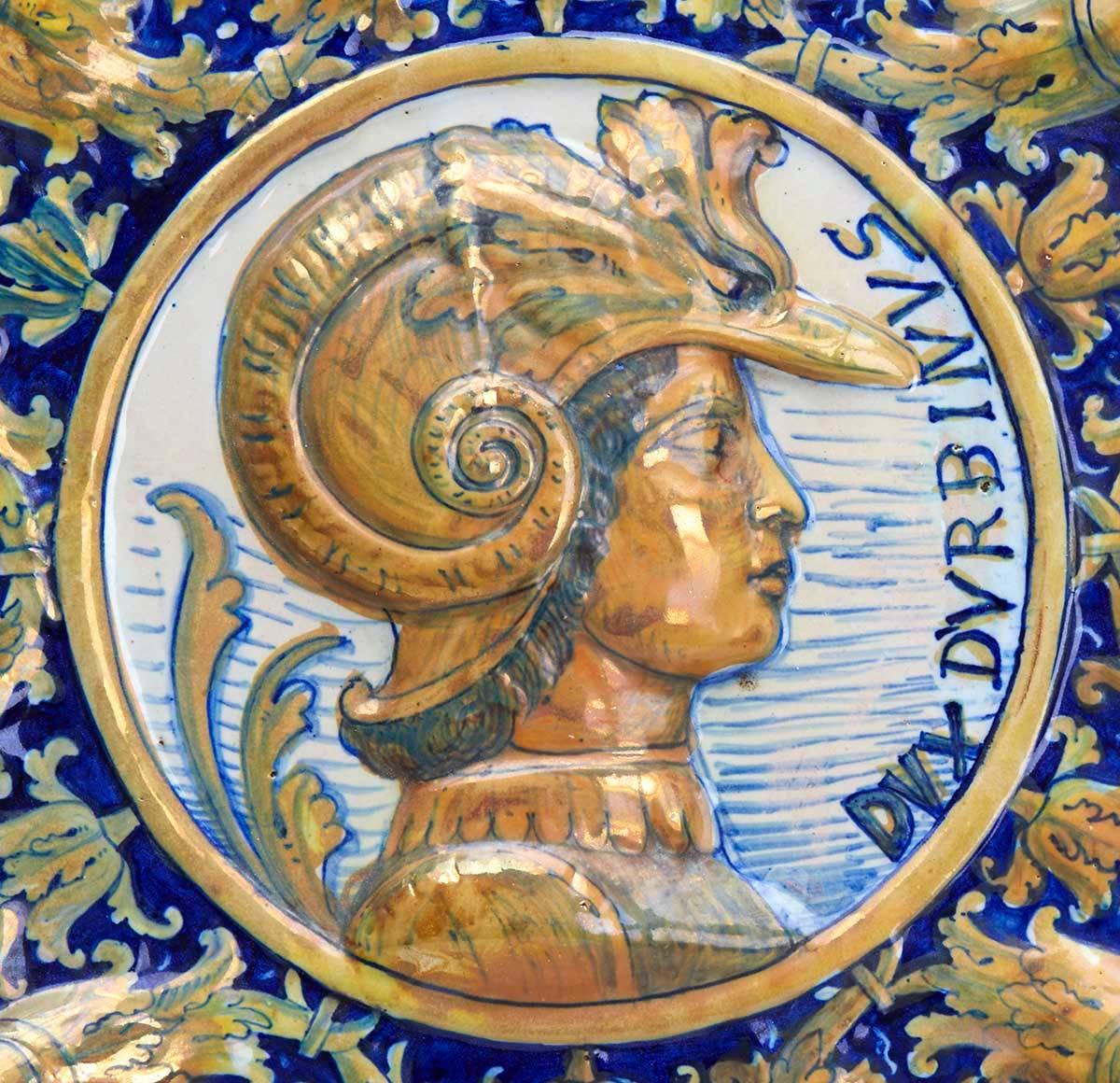 Eine hervorragende antike, reliefgeformte kontinentale Maiolica-Schale oder -Plakette mit einem seitlichen Profilporträt einer Figur, die einen Militärhelm trägt, und mit der Aufschrift DUX D'URBINUS an der Seite. Das zentrale Porträt ist von einem