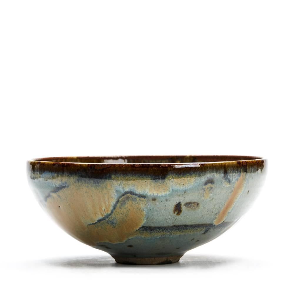 A stylish vintage stoneware Studio Pottery bowl or rounded form standing on a narrow rounded unglazed foot and decorated in coloured glazes with textured rust like inclusions. The bowl has an incised signature to the base, an impressed monogram to