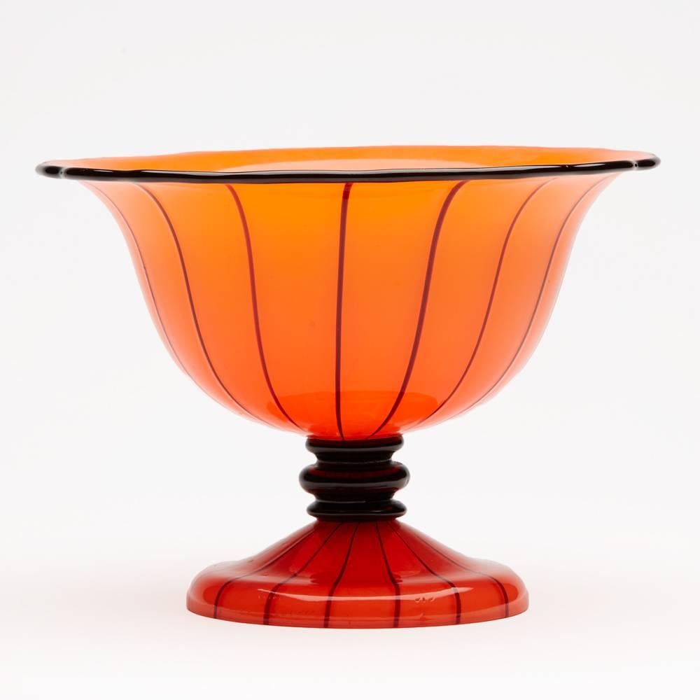 A stylish Michael Powolny cased tango orange glass pedestal bowl with black piping and stem made by Loetz. The hand blown bowl stands on a rounded pedestal foot with a short 'black' glass ring stem with wide rounded bowl top with black piped edge