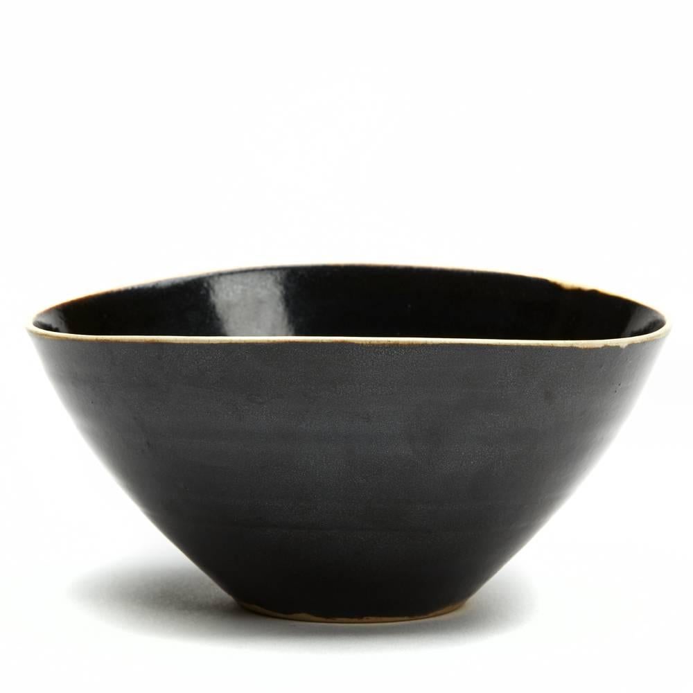 A stunning vintage British Studio Pottery bowl by Lucie Rie and Hans Coper, thinly thrown and decorated in black glaze with a white glazed rim. The bowl is slightly 'squeezed' in shape and stands on a narrow rounded unglazed foot rim with impressed