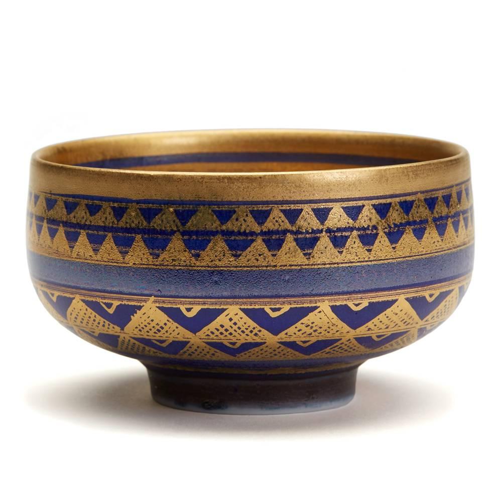 A very fine and stylish studio pottery bowl of wide rounded form standing on a narrow rounded foot and finely decorated with a richly gilded geometrical pattern on a deep blue ground in Islamic style crystalline glazes. The porcelain bowl has an