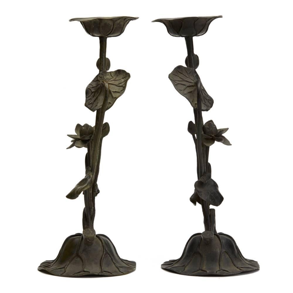 A fine and stylish pair Japanese bronze signed candlestick modeled as Lotus flowers the base moulded as a large leaf with a flowering stem column and wide leaf shaped candle holder. Both have a wonderful age patina and both have incised makers