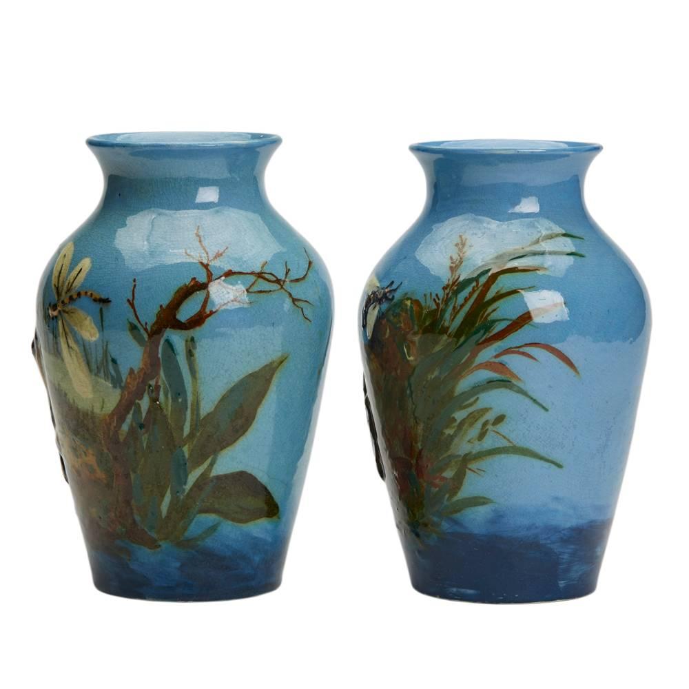 A very rare pair of Burmantofts Faience Barbotine vases decorated in low relief with frogs seated at the edge of a pond hunting insects, one watching a dragon fly and the other a fly and a beetle crawling up a nearby floral stem by Harold Leach. The