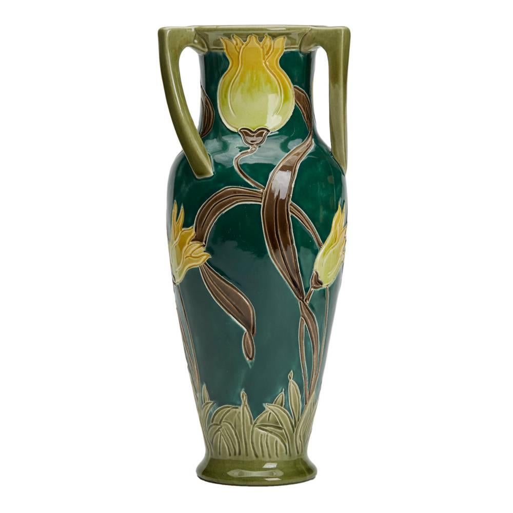 A stunning Art Nouveau Burmantofts faience vase of tall elegant form with three twisted handles, the body decorated incised tube-lined style tulips in yellow brown and green on a bottle green ground. The vase is numbered 2247 and has various