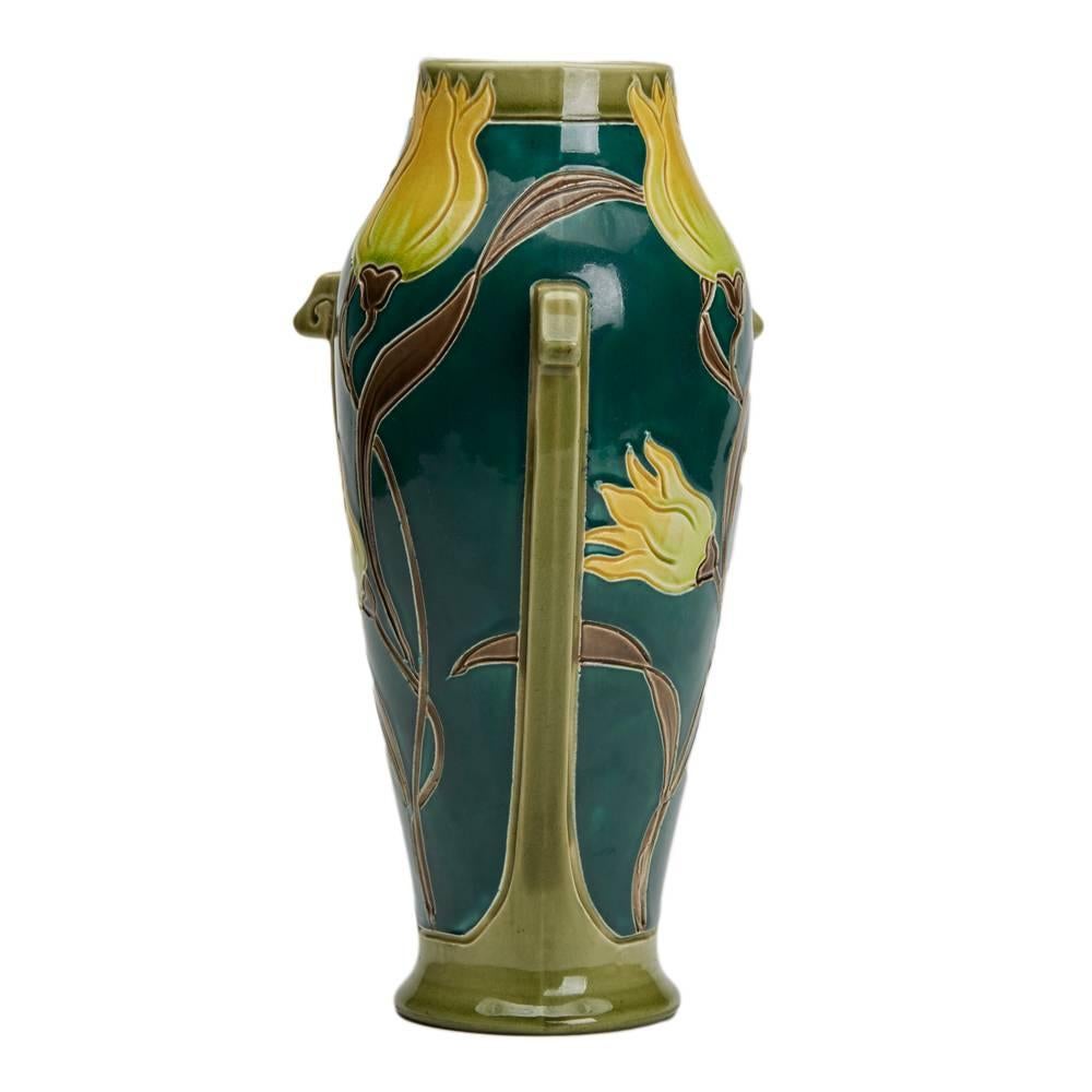 A stunning Art Nouveau Burmantofts Faience vase of tall elegant form with three small protruding handles, the body decorated incised tube-lined style tulips in yellow brown and green on a bottle green ground. The vase is numbered 2246 and has